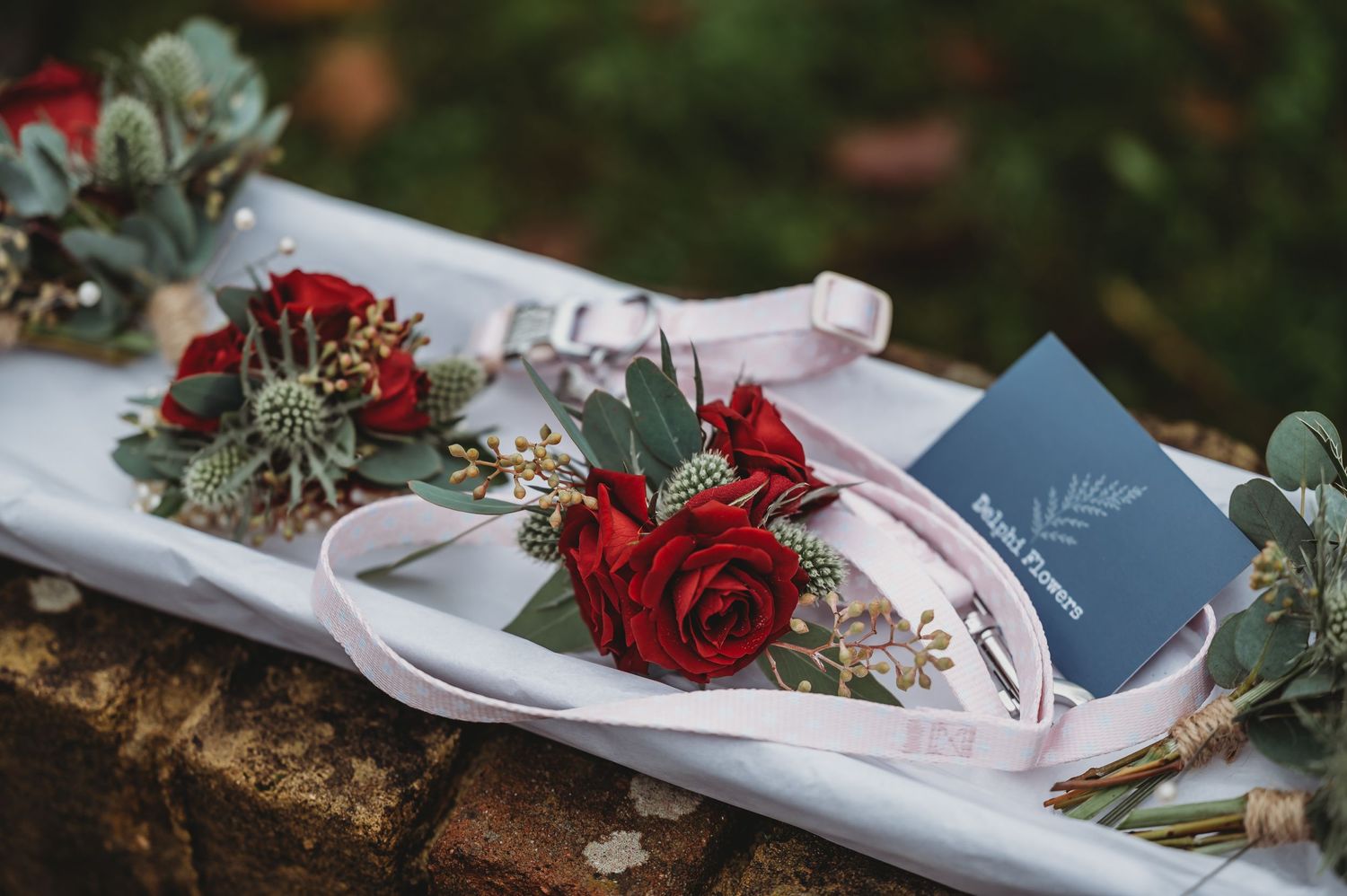 Wedding florals featuring red roses and eucalyptus leaves arranged with pink ribbon.