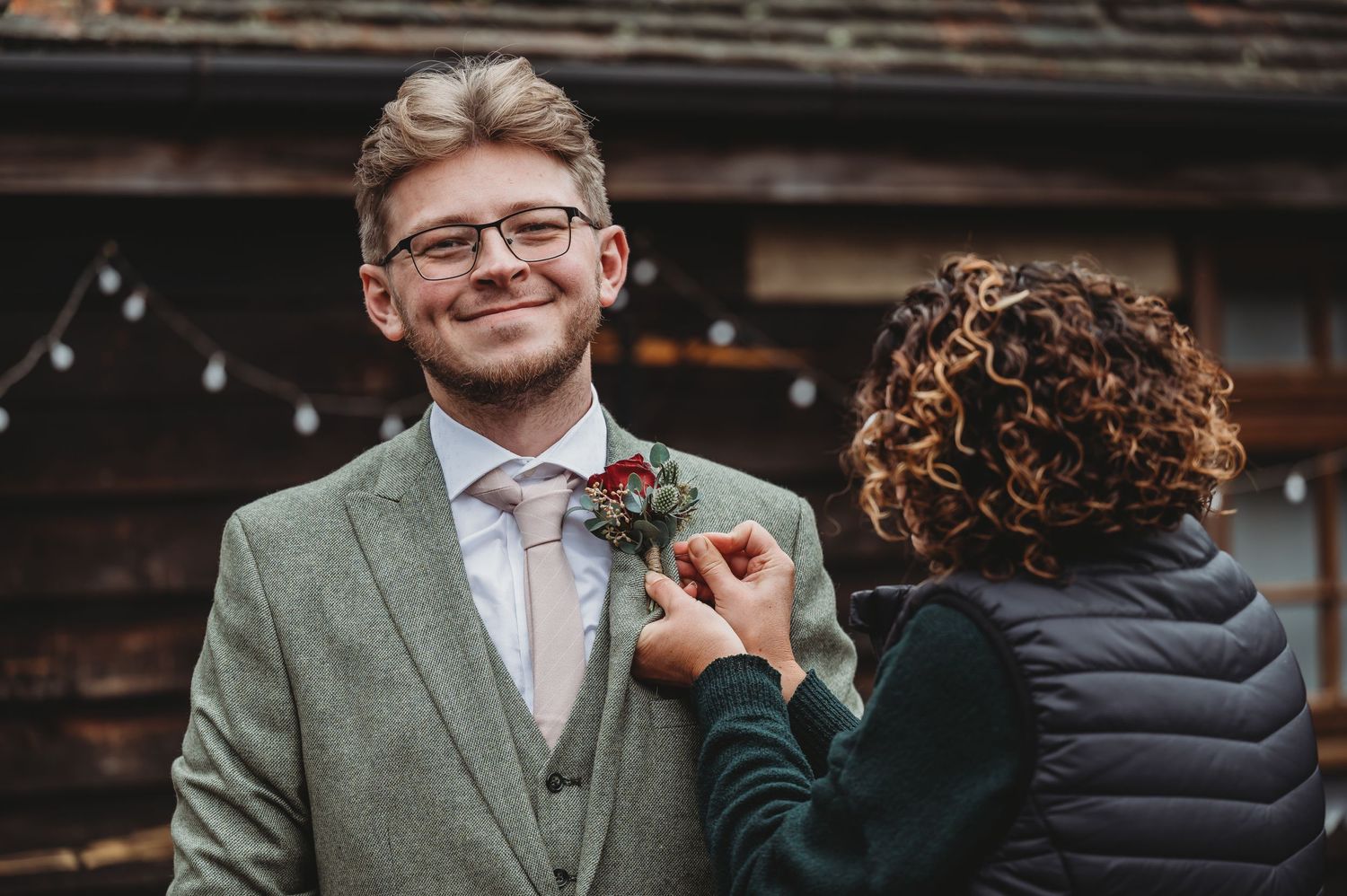 A boutonniere being pinned onto a sage green suit jacket outdoors.