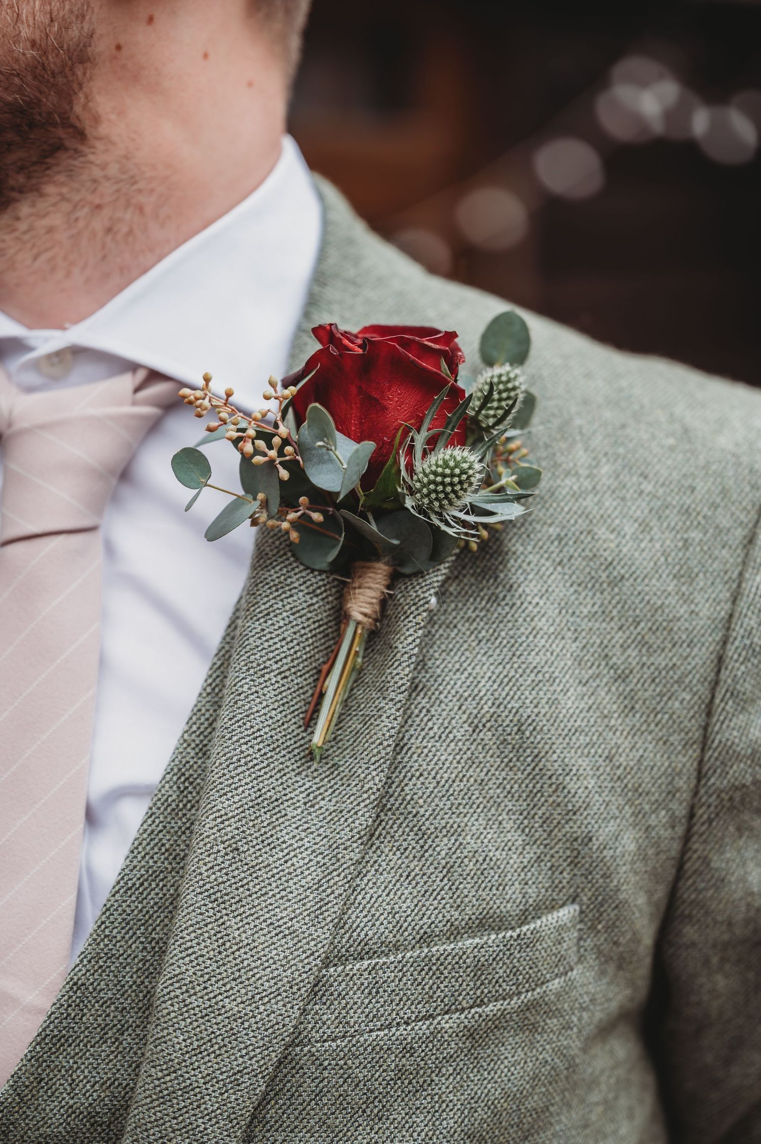 A red rose and thistle boutonniere pinned to a grey tweed suit jacket lapel.