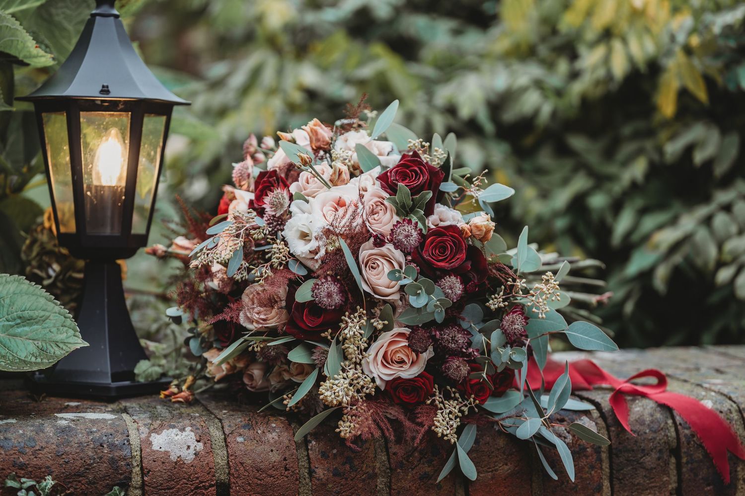 Vintage garden wedding bouquet with pink and burgundy flowers next to antique lantern.