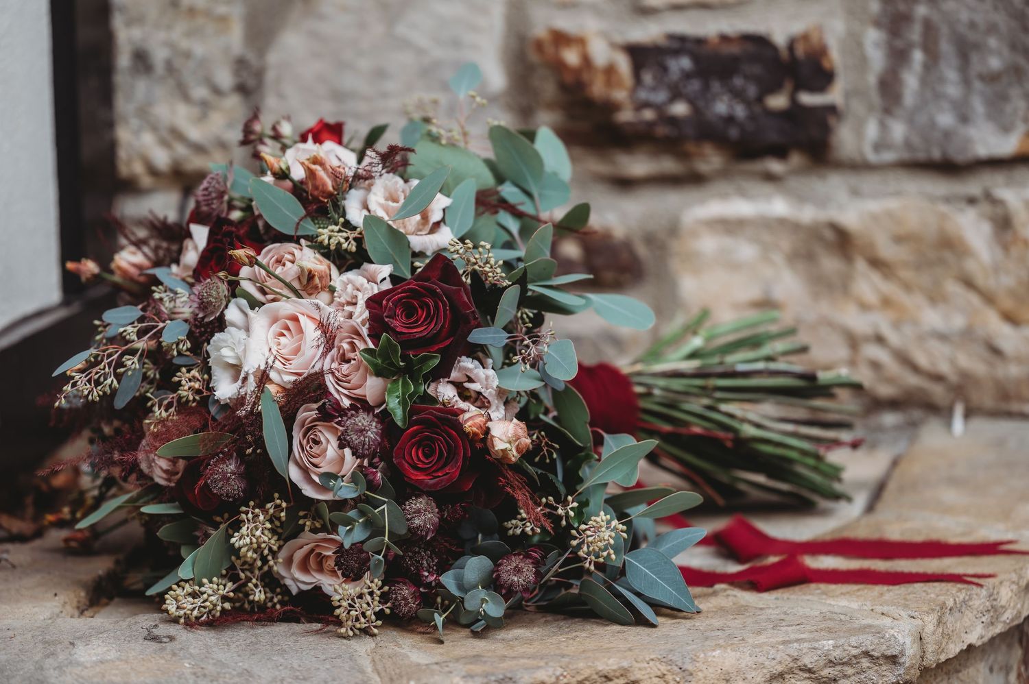 Romantic wedding bouquet with burgundy and pink roses mixed with eucalyptus on stone surface.