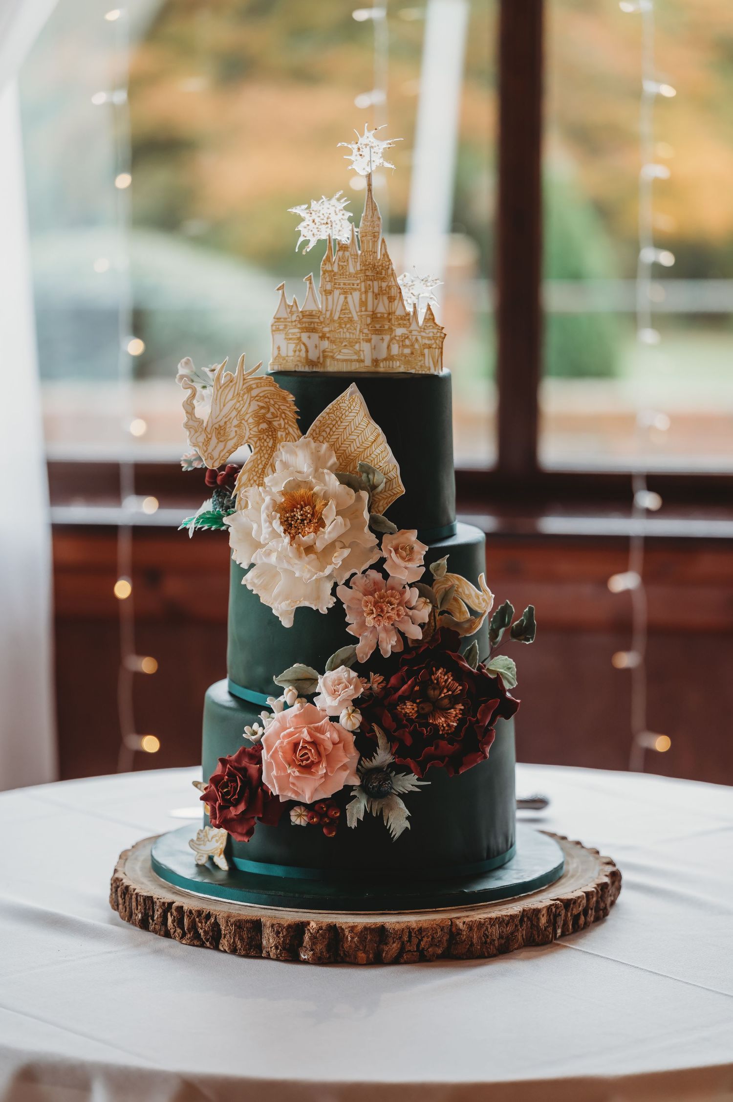 Tiered dark green wedding cake adorned with castle topper and peachy floral decorations.