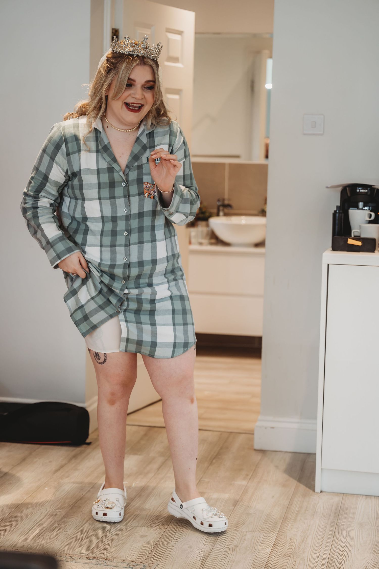 A joyful moment in plaid pajamas and slippers while wearing a tiara in a modern kitchen.