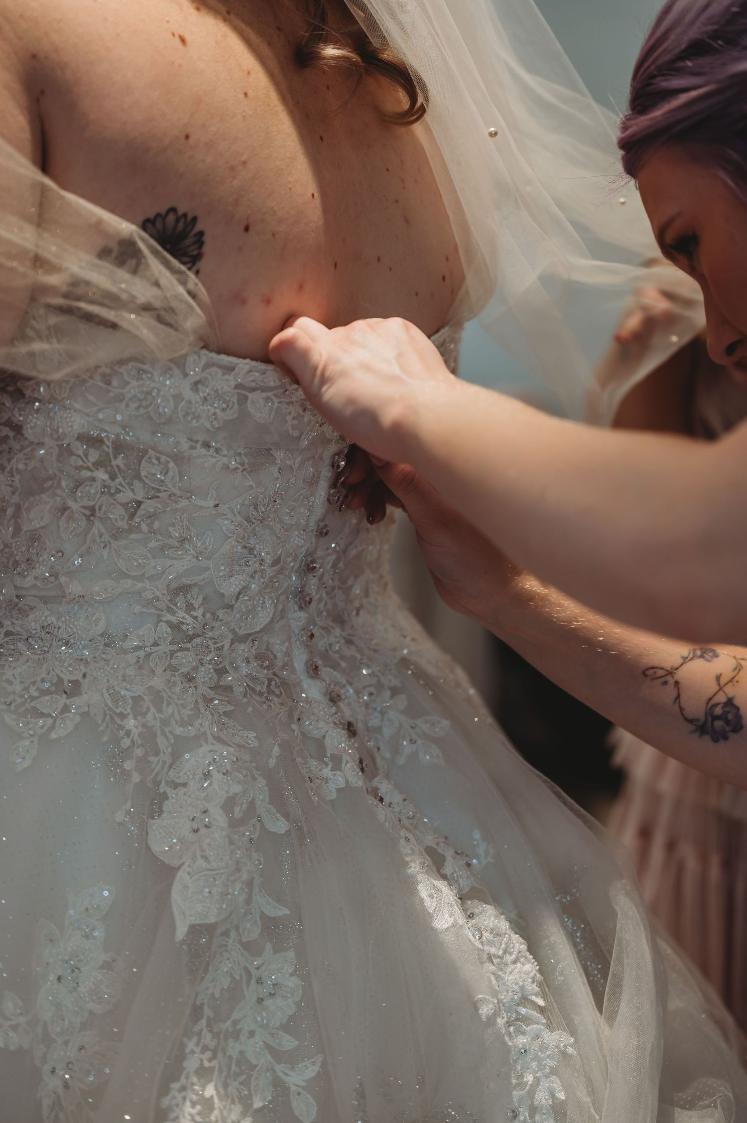 Detailed shot of hands adjusting the intricate lace detail on a white wedding dress.