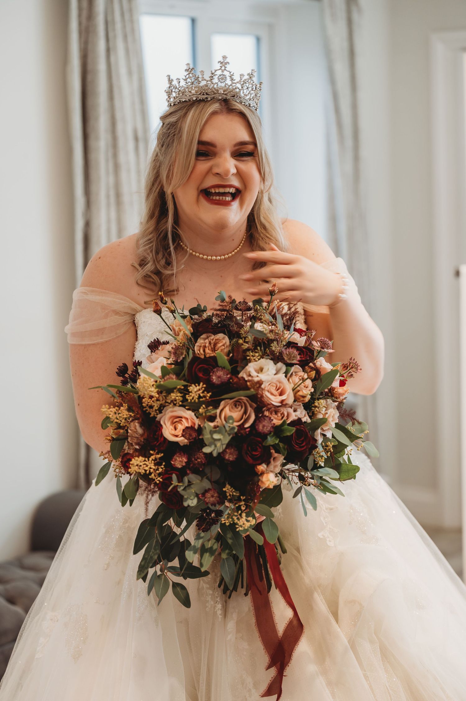 Joyful bridal moment featuring ornate tiara and lush autumn-toned bouquet.