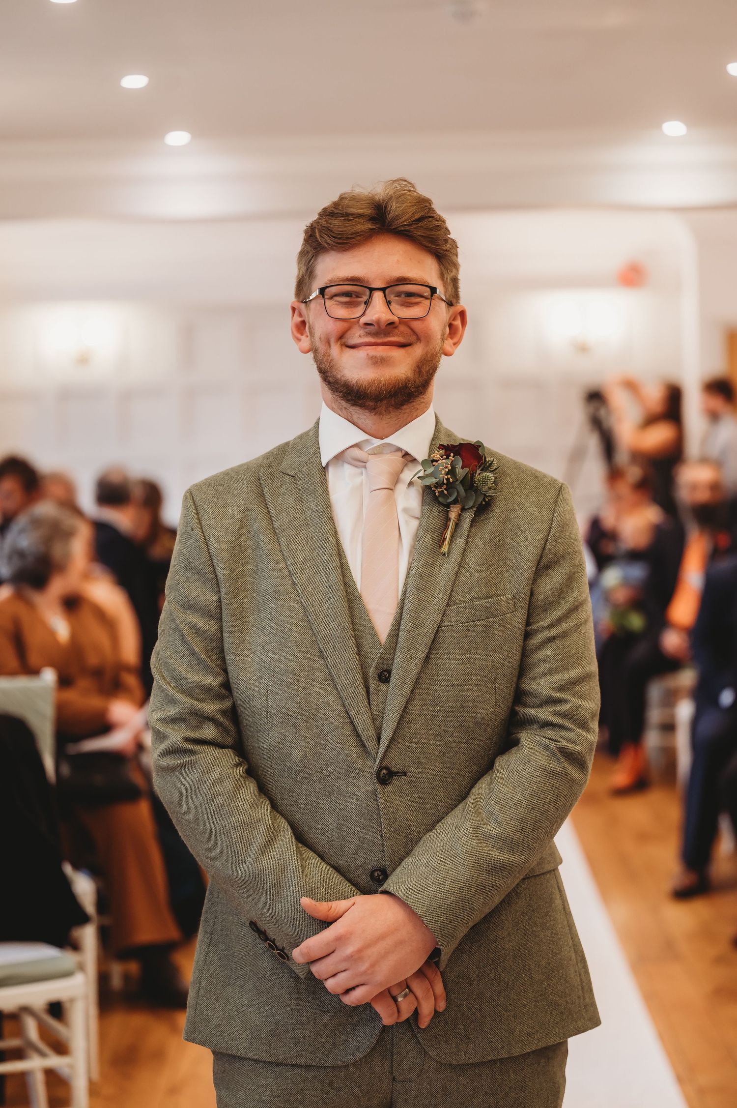 Wedding ceremony scene in a bright white venue with formal attire and floral boutonniere.