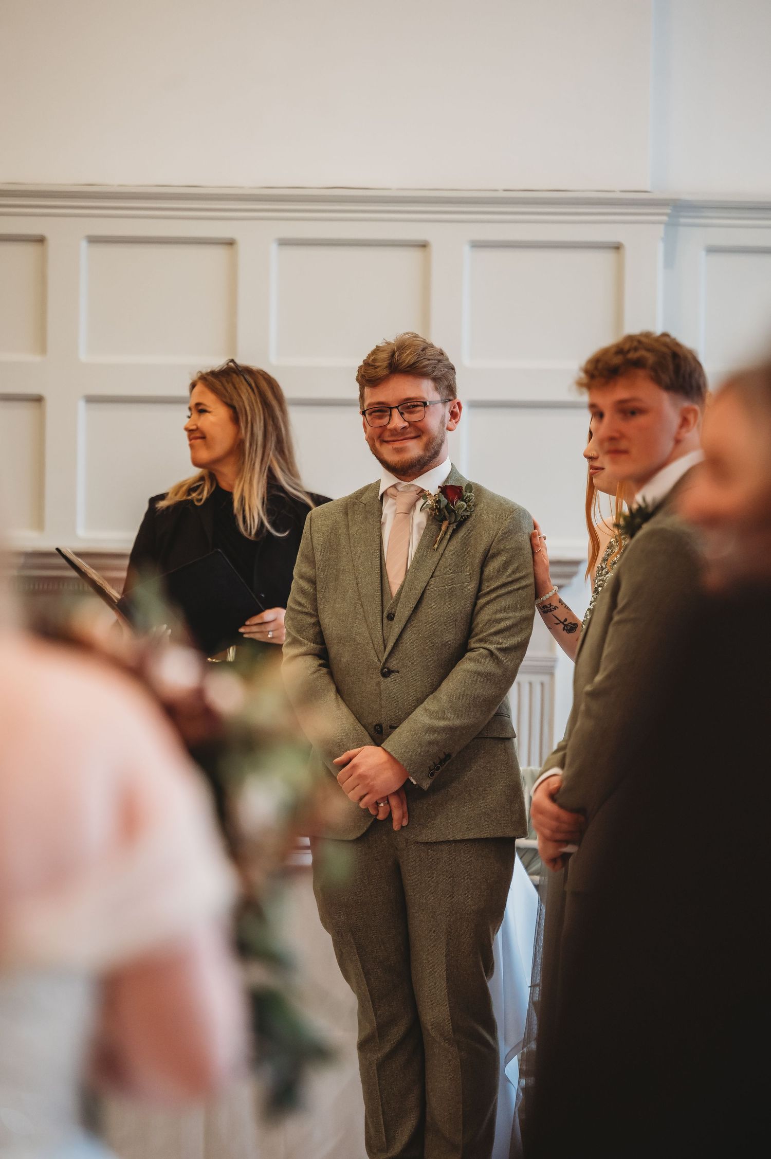 Wedding party members stand at the altar in a classic white-walled ceremony space.