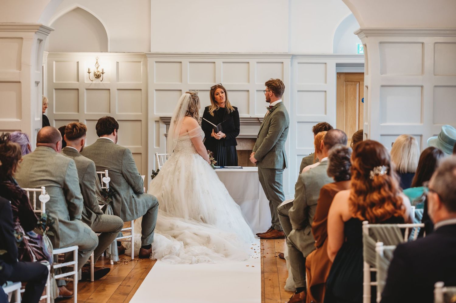 A wedding ceremony in a bright chapel-like room with arched doorways and white paneled walls.