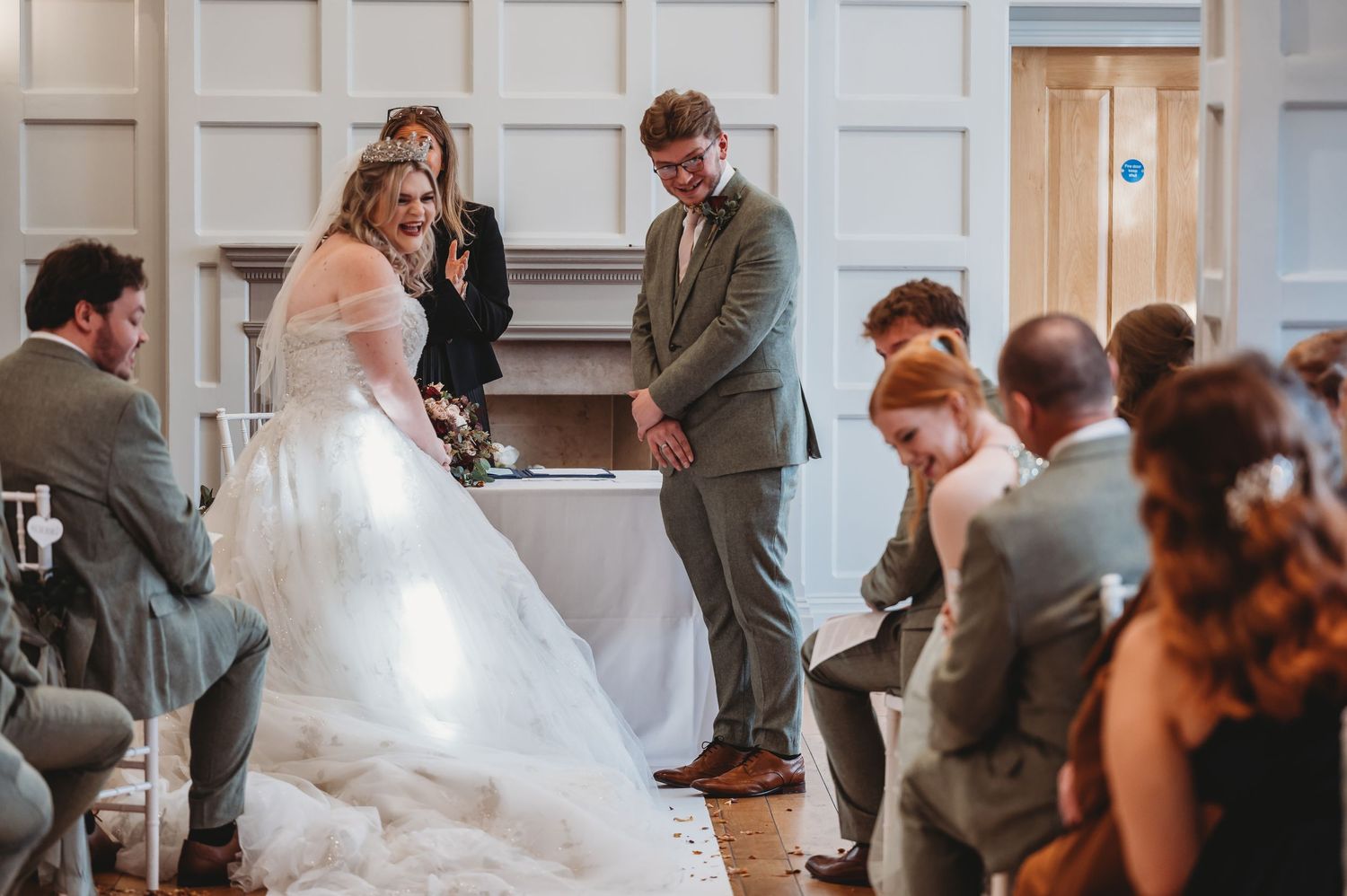 A wedding ceremony in progress with guests seated on white chairs in an elegant room.