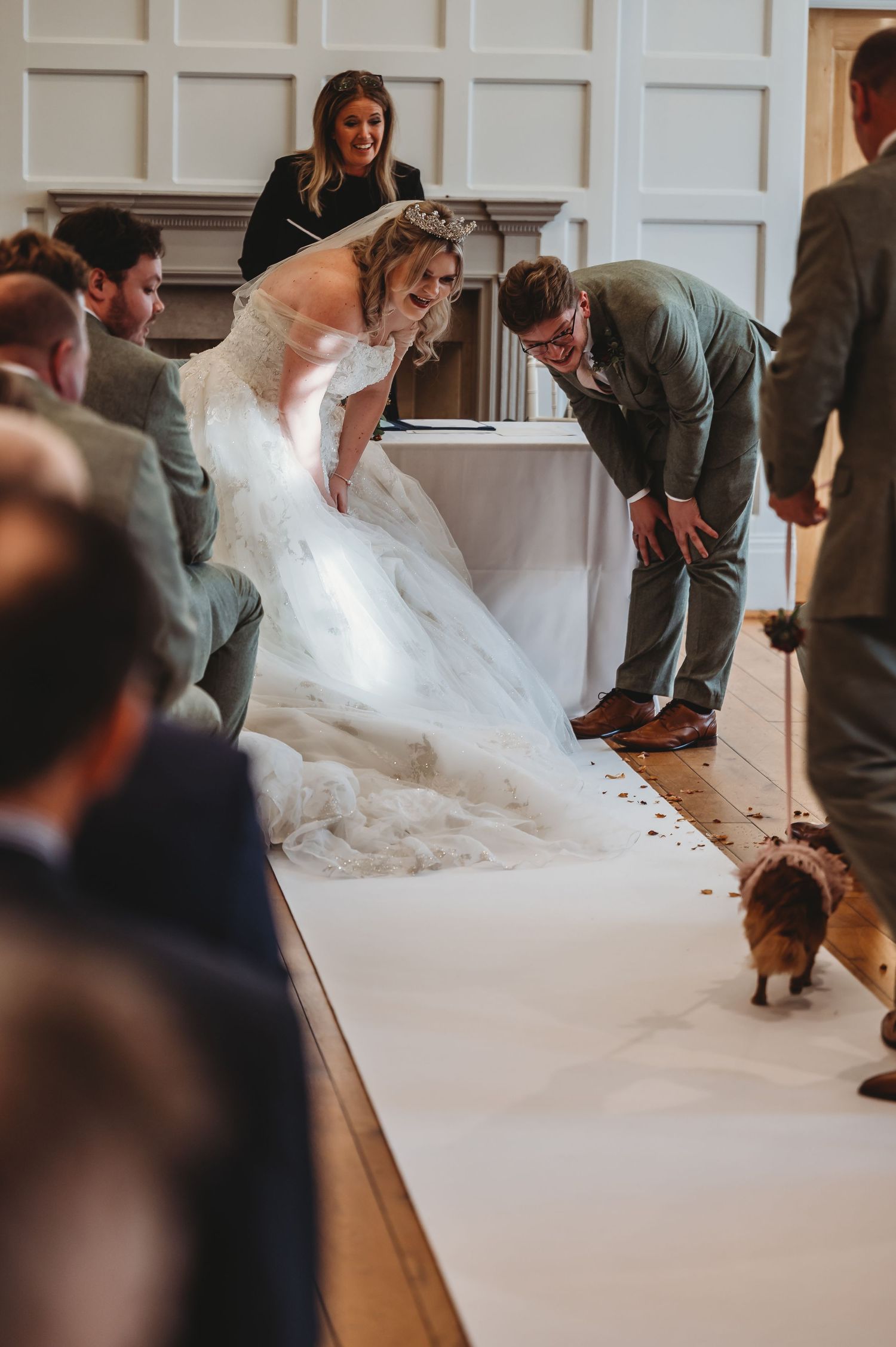 A playful moment during a wedding ceremony as attendees look down at something on the floor.