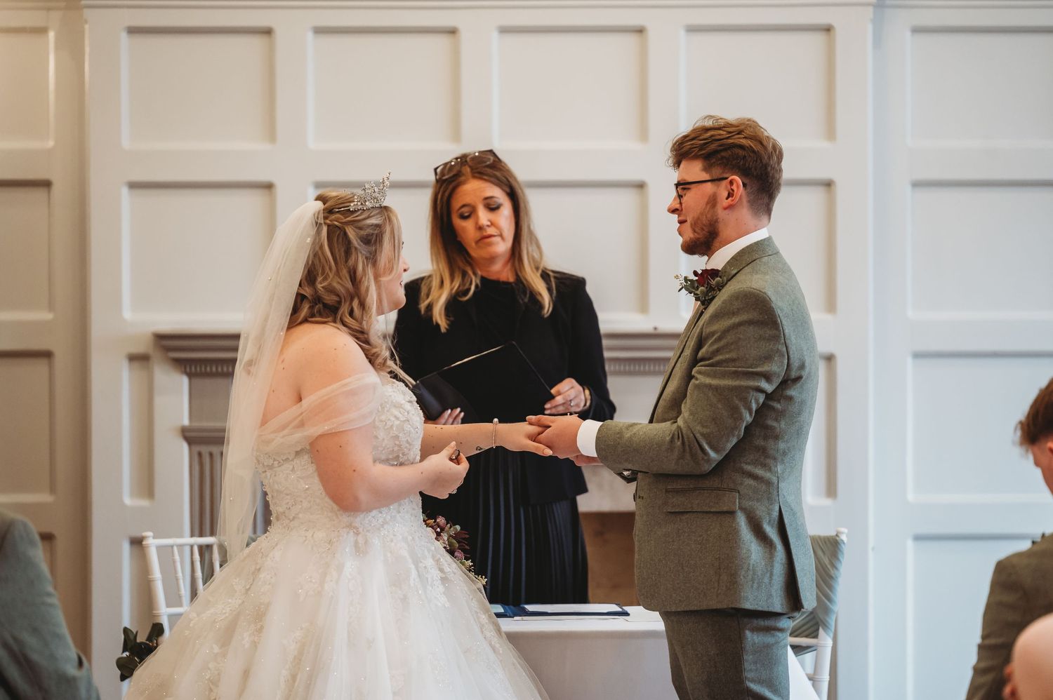 An intimate wedding ceremony moment with the couple and officiant against white paneled walls.