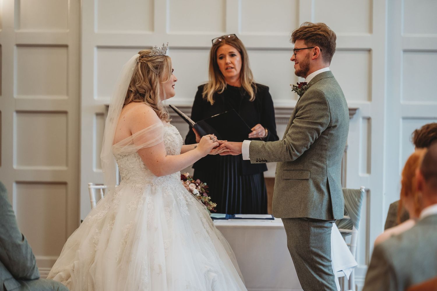A couple exchanges wedding vows in front of an officiant during their indoor ceremony.