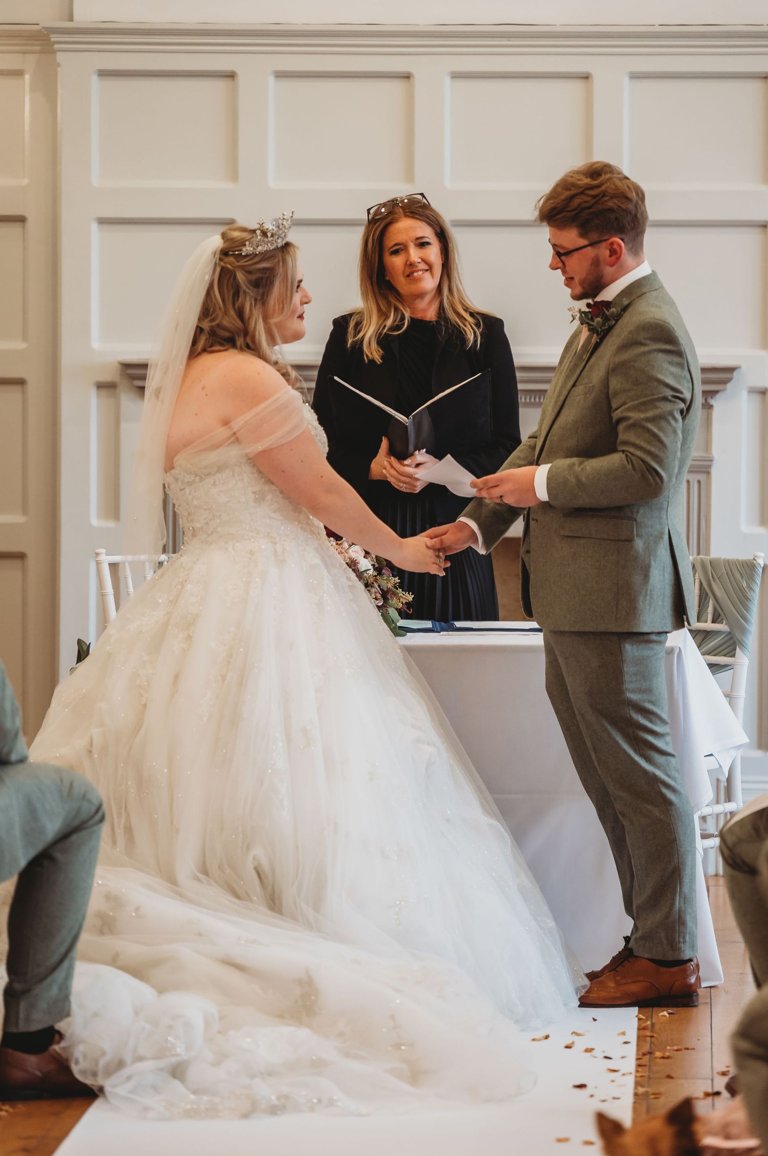 A wedding ceremony taking place in an elegant white-paneled room with the couple exchanging rings.
