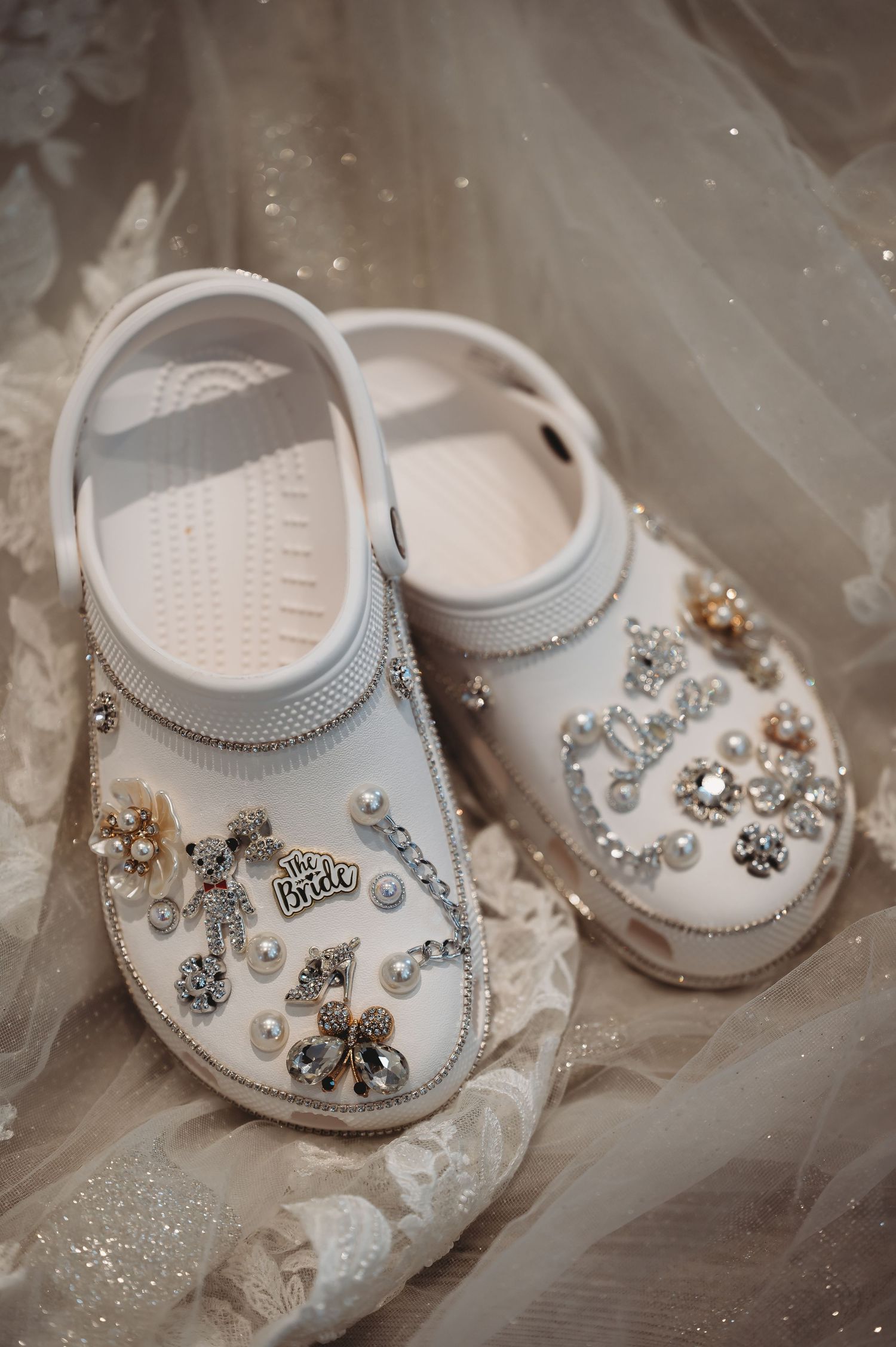 Decorative white Crocs shoes adorned with pearls and rhinestones on tulle fabric.