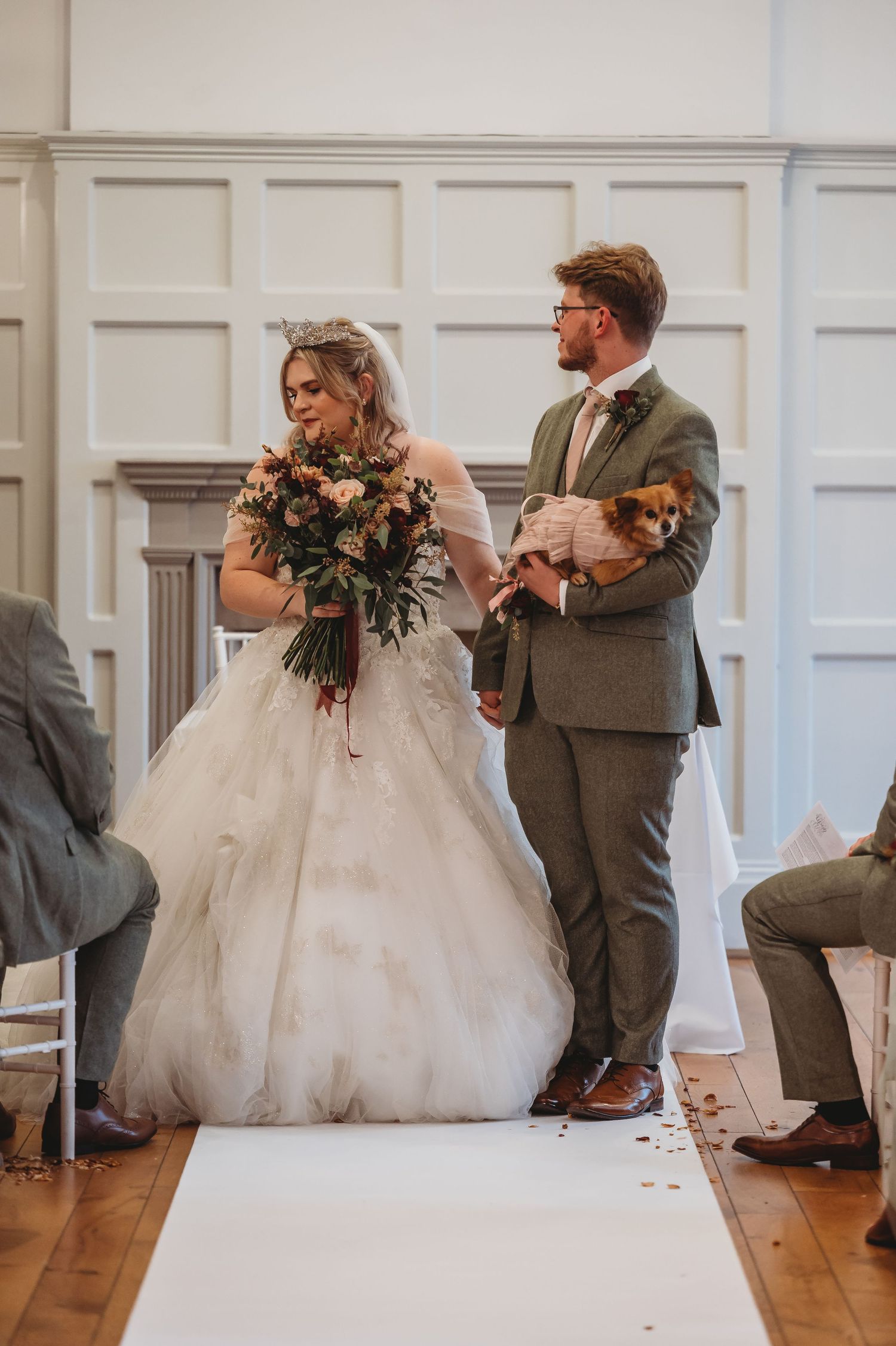 Couple stands on white aisle runner during wedding ceremony in classic white-paneled room.