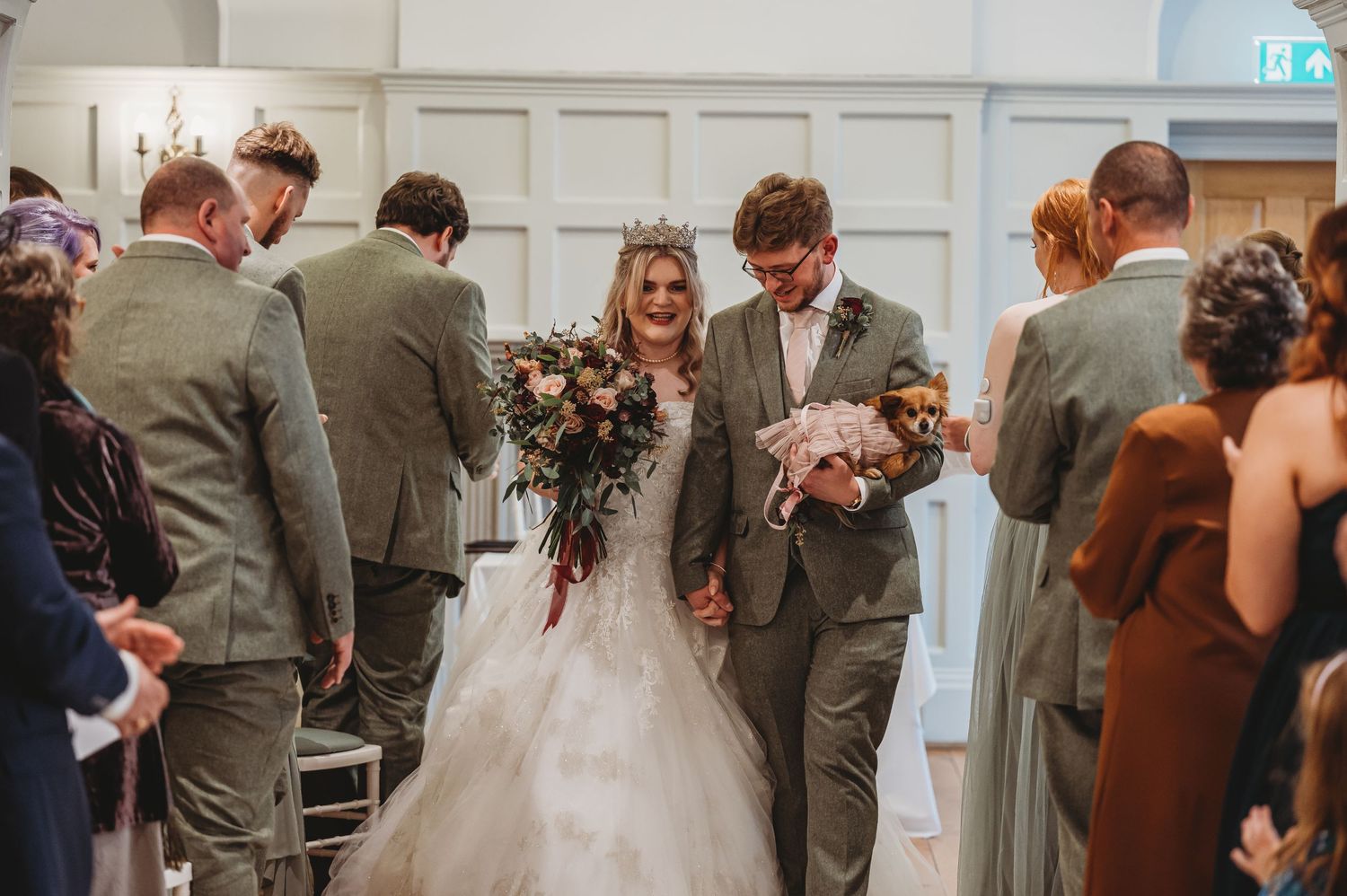 Wedding celebration in progress with guests lining the aisle in an elegant white-paneled venue.