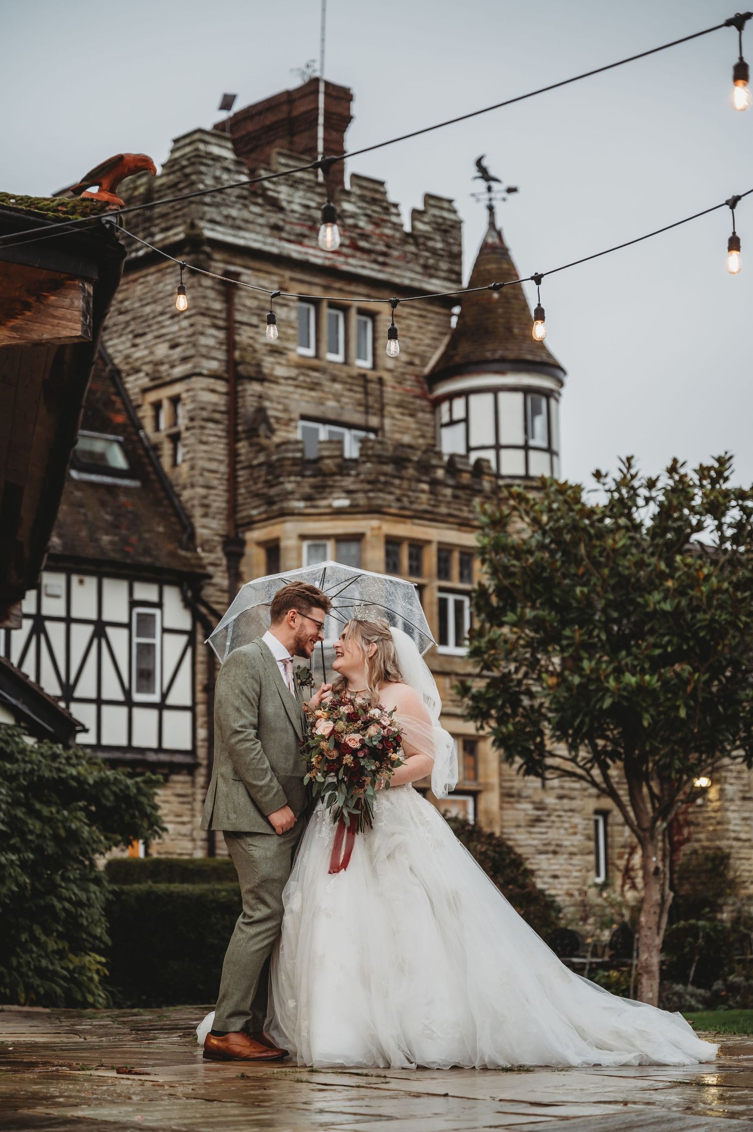 Wedding couple posing in front of a beautiful stone castle with Tudor architectural details.