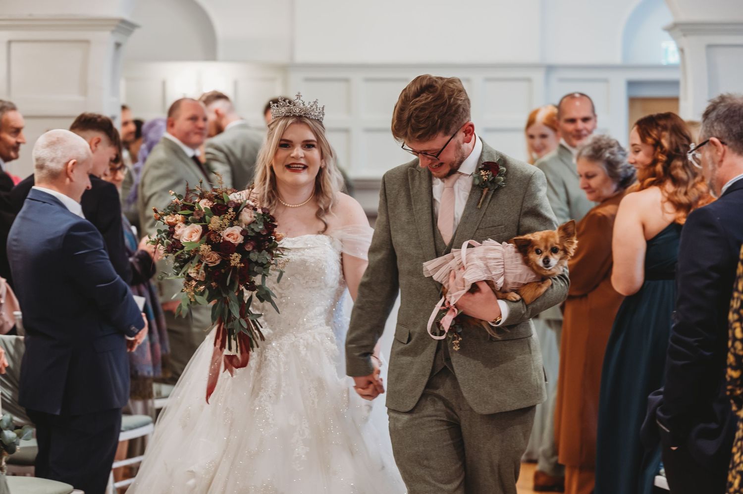 Newlyweds celebrate joyfully while walking down the aisle in an elegant white church setting.