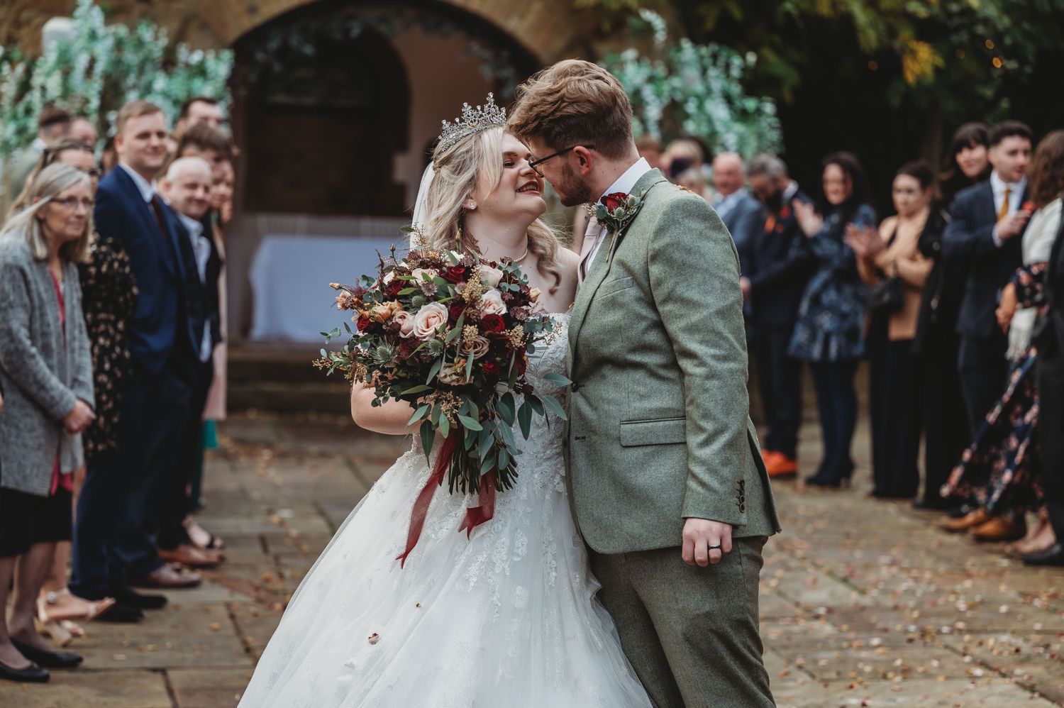 Romantic wedding kiss in front of stone church while guests look on.