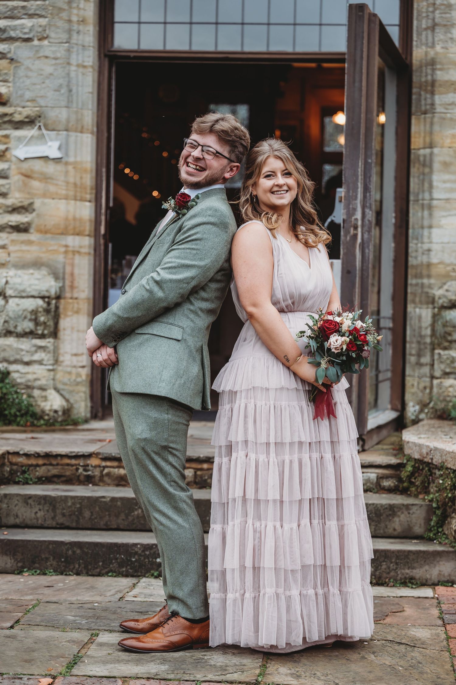 Wedding couple poses back-to-back on stone steps in coordinating formal attire.