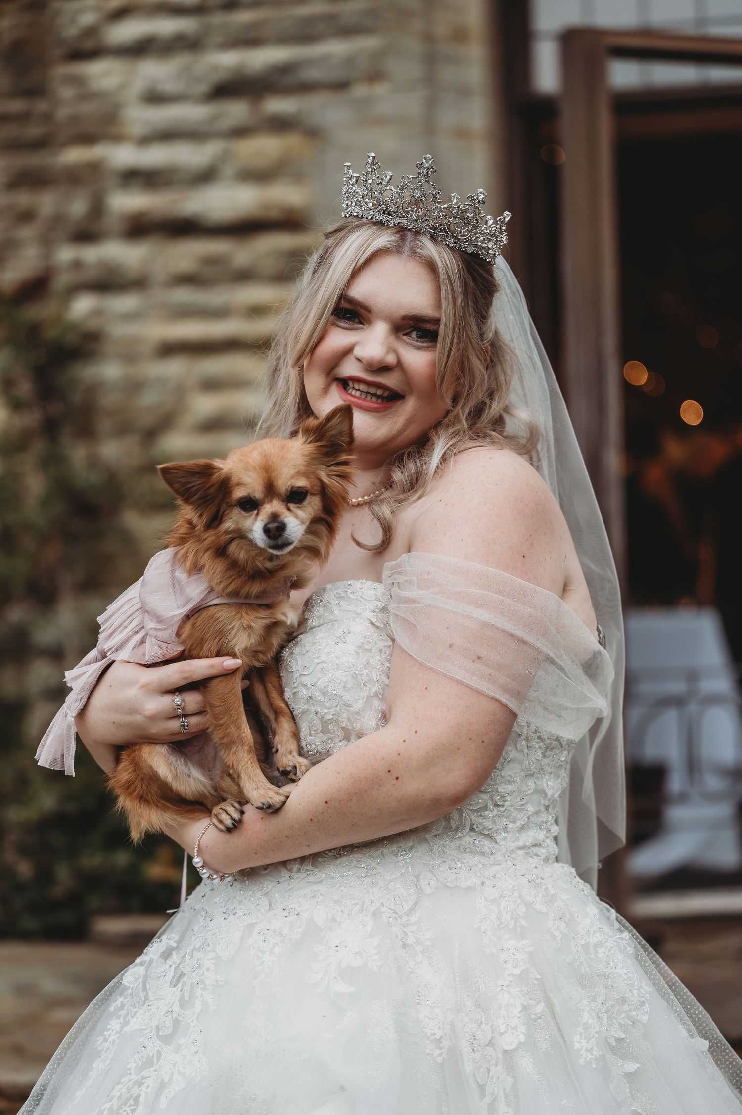 A wedding portrait featuring a bride in a white gown holding a small Chihuahua mix dog.
