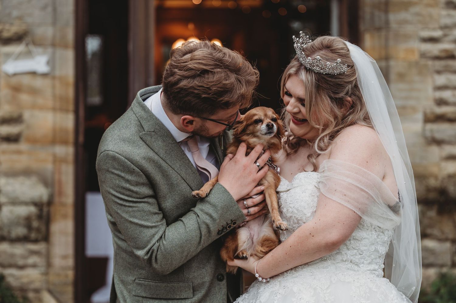 Tender moment as newlyweds cuddle their small dog during wedding portraits.