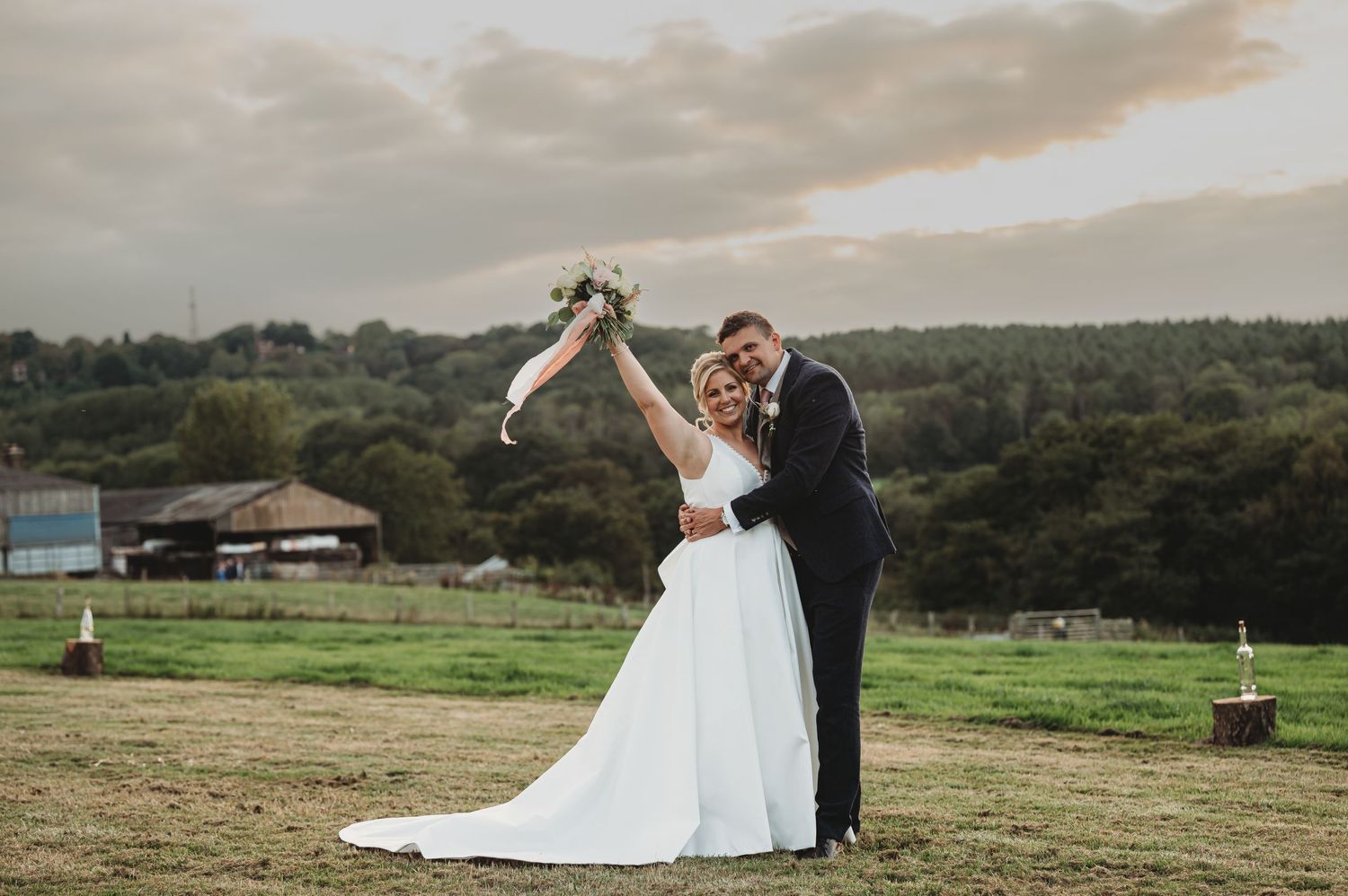 A bride and groom dance together on a hilltop with a scenic countryside view during golden hour.