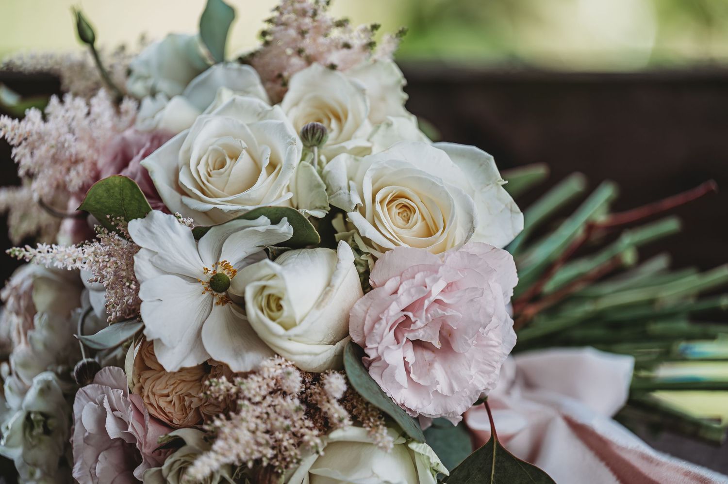 A romantic wedding bouquet featuring white roses and soft pink blooms tied with ribbon.