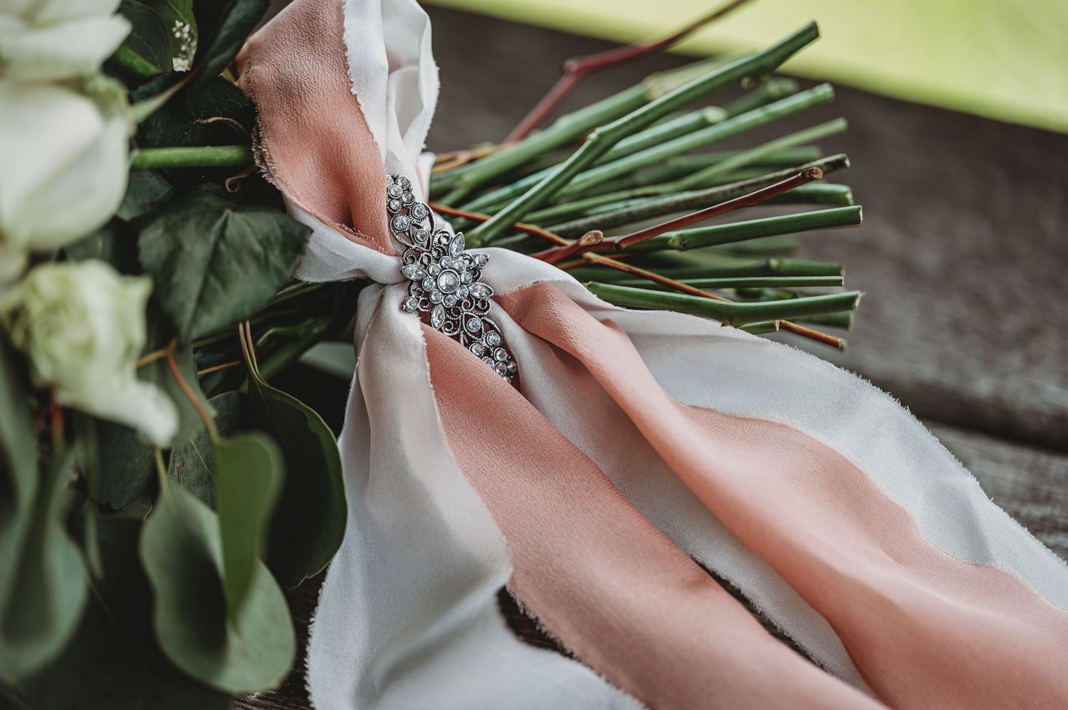 Close-up of a bridal bouquet wrapped with pink and white ribbons secured by a decorative silver brooch.