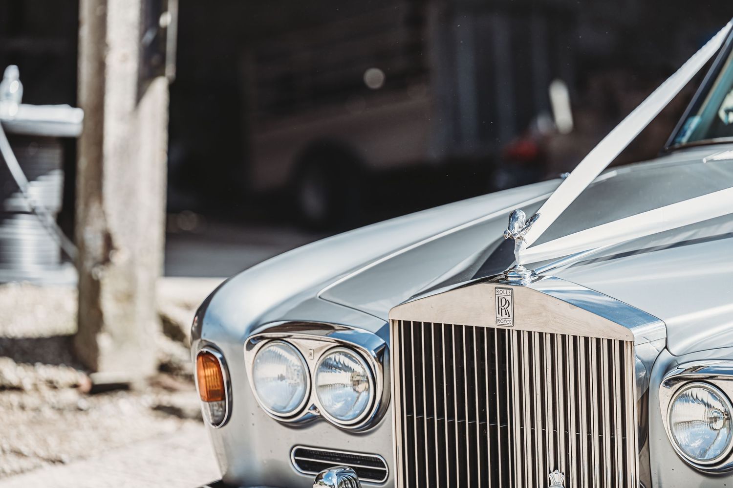 Close-up detail shot of a classic silver Rolls Royce front grille and headlights against a blurred background.