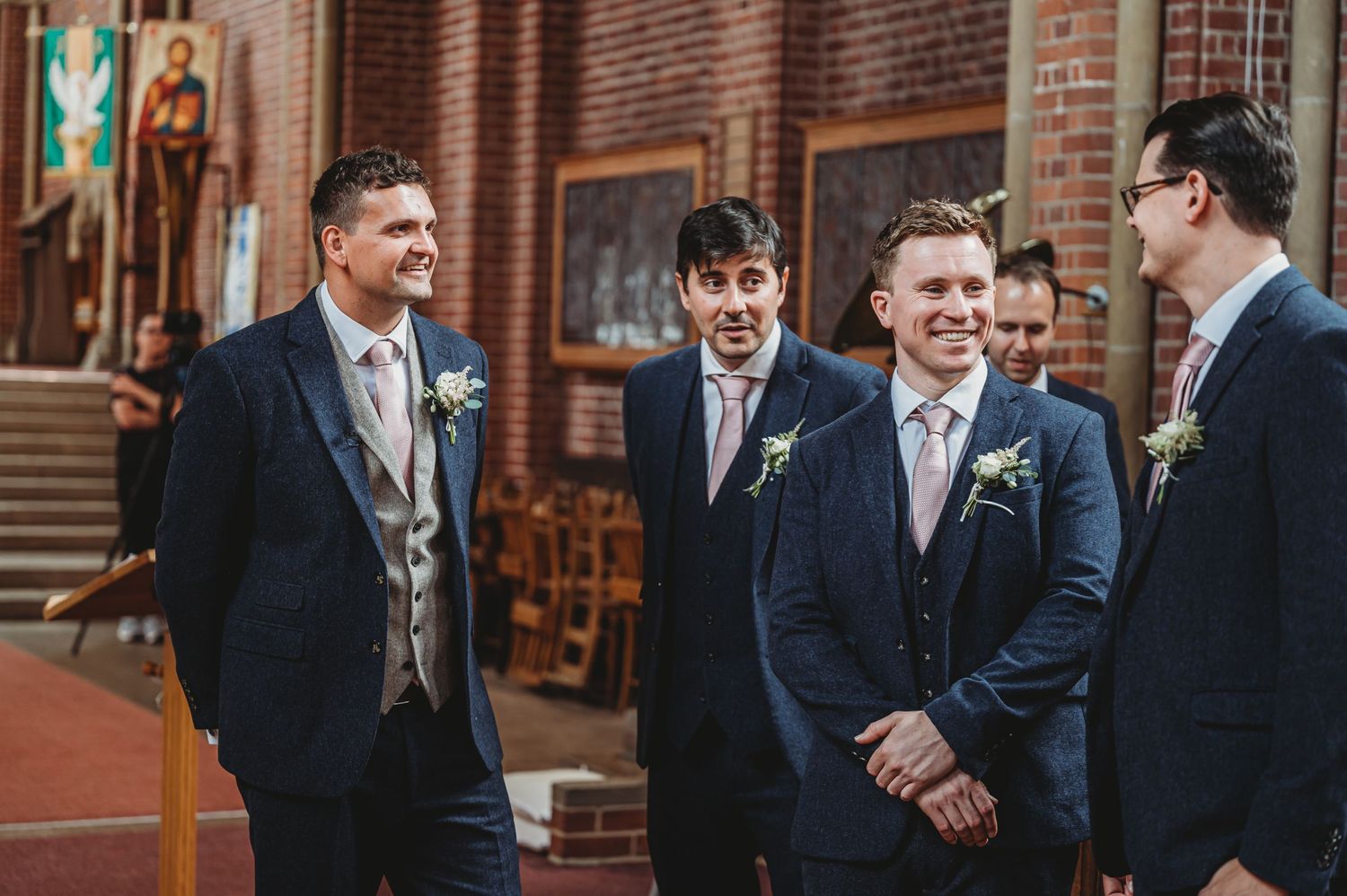 A group of formally dressed attendants share a joyful moment at the altar inside a brick church during a wedding ceremony.