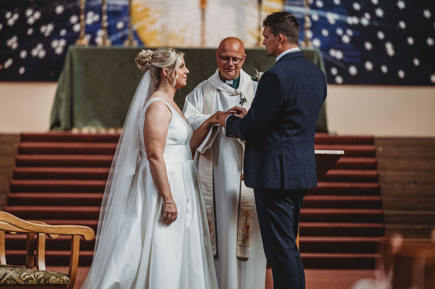 A wedding ceremony takes place inside a church with a minister performing the service at the altar steps.