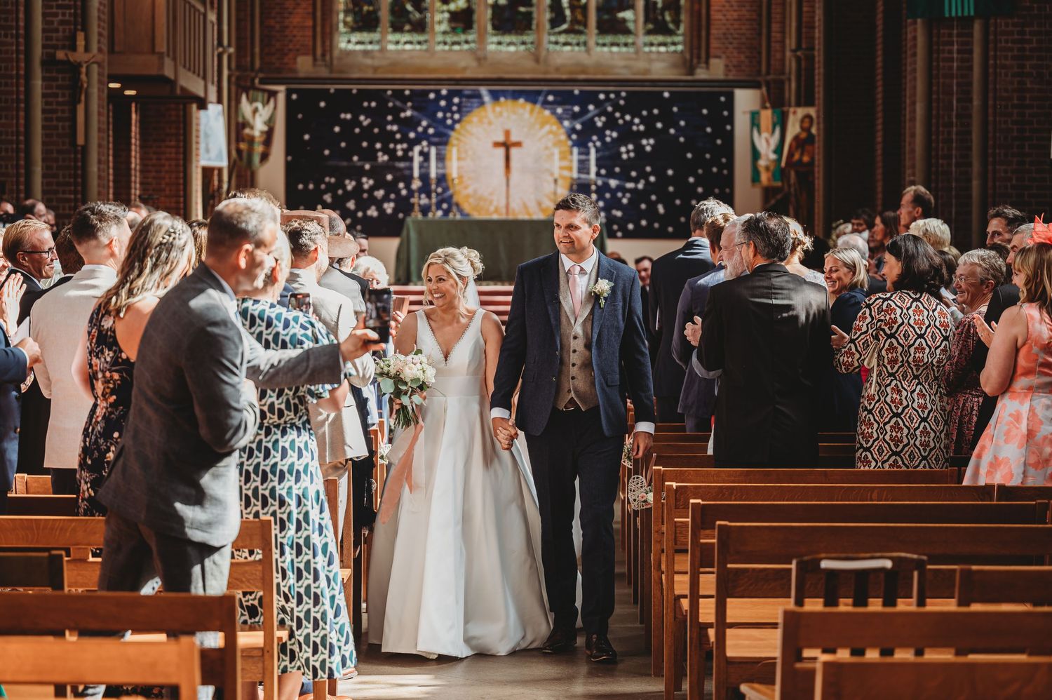 Wedding guests rise from church pews during ceremony with cross and American flag decorating the altar area.