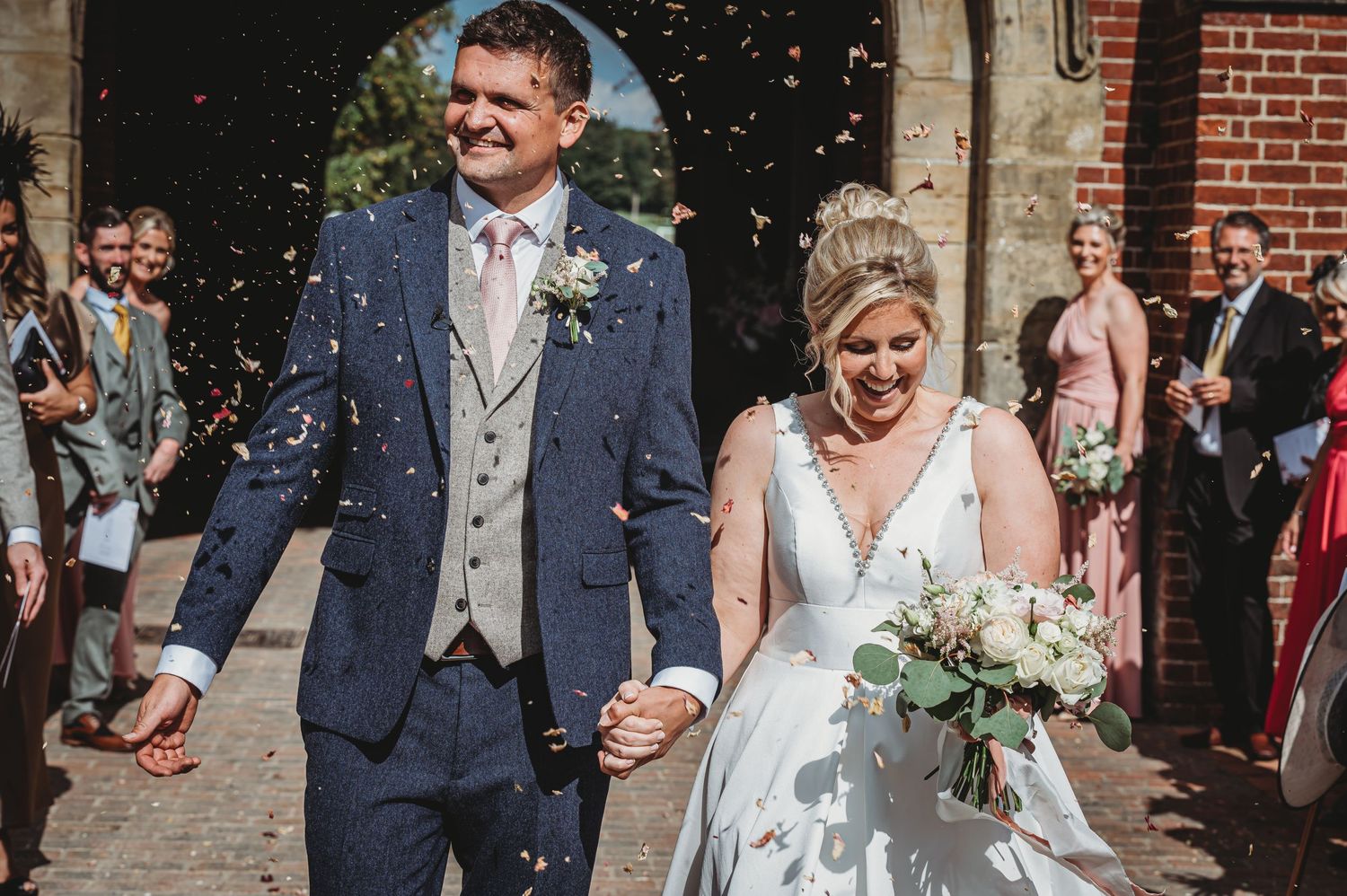 A joyful newlywed couple exits their wedding ceremony while guests shower them with confetti on a sunny day.
