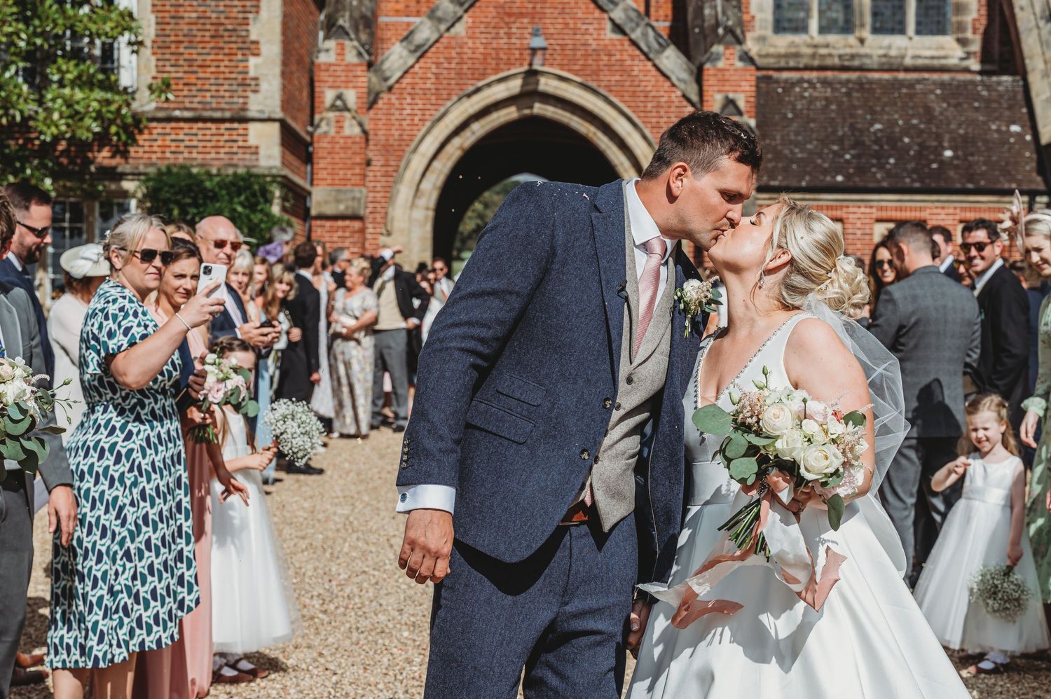 A joyful couple shares a special moment outside a historic brick church surrounded by guests on their wedding day.