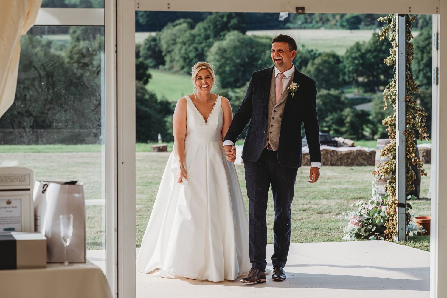 A couple stands under an elegant outdoor porch on their wedding day, with the bride in a white gown and groom in a suit.