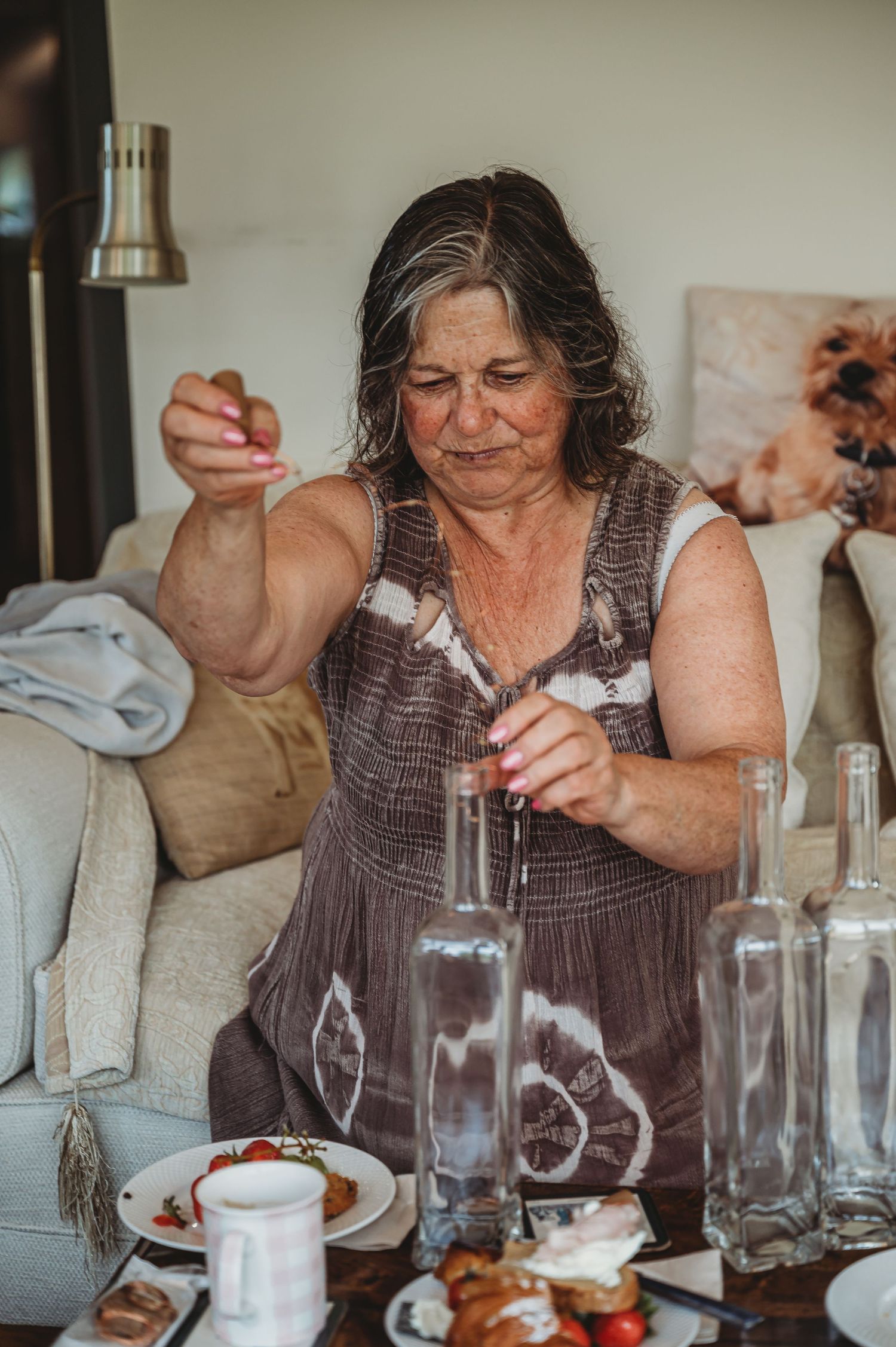 Someone in denim overalls works meticulously with glass bottles and platters at a casual dining table setting.