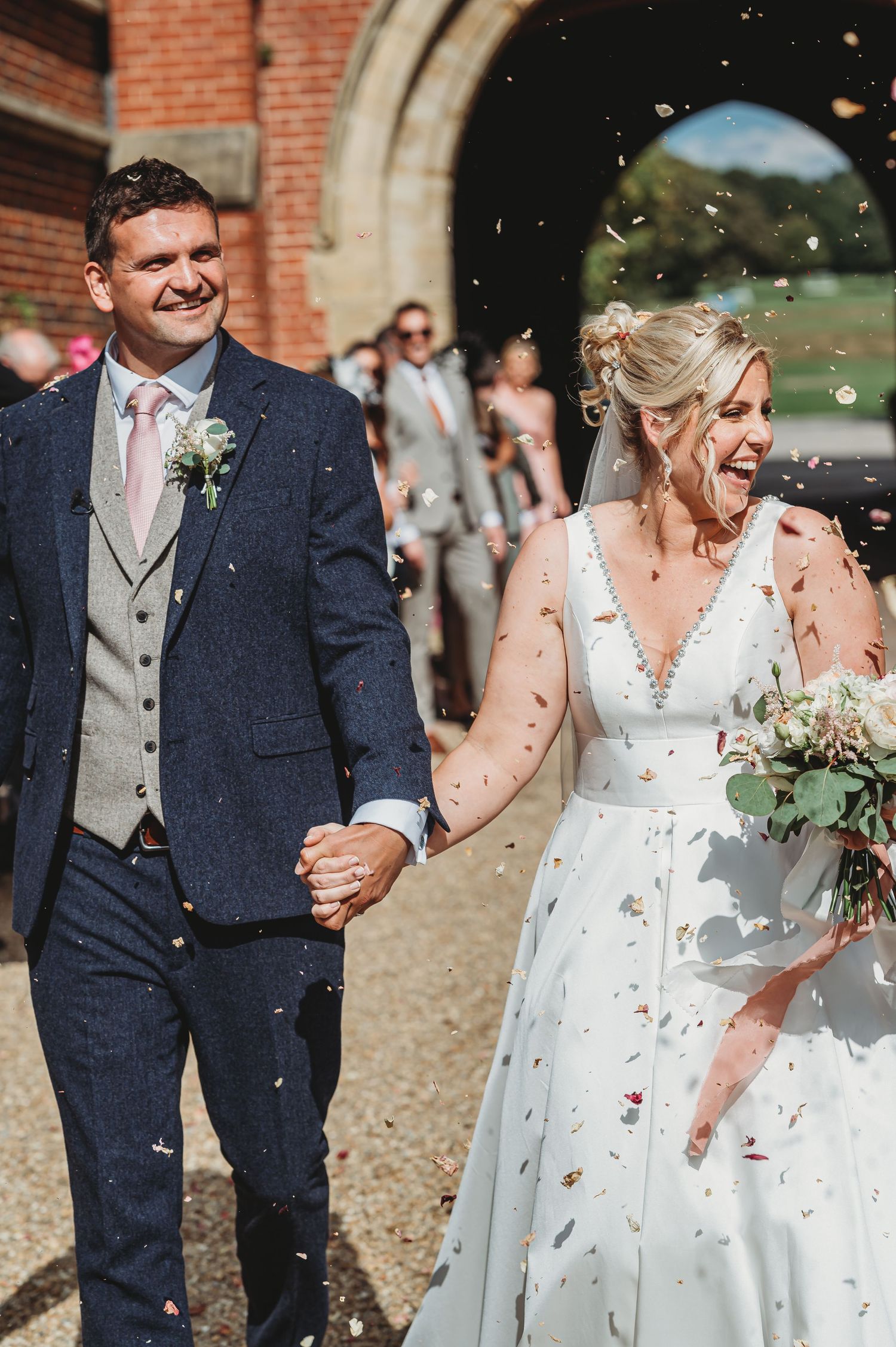 A happy bride and groom exit their wedding ceremony while guests throw confetti outside a brick church.