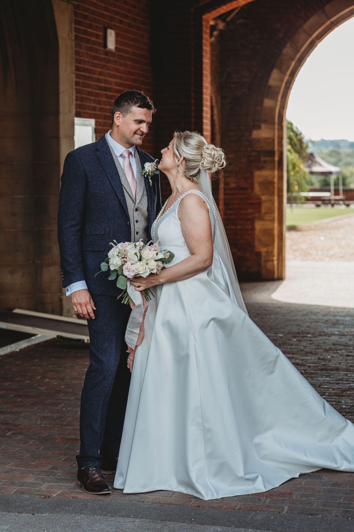 A romantic wedding moment captured in a brick archway as the couple shares a tender moment with white floral bouquet.