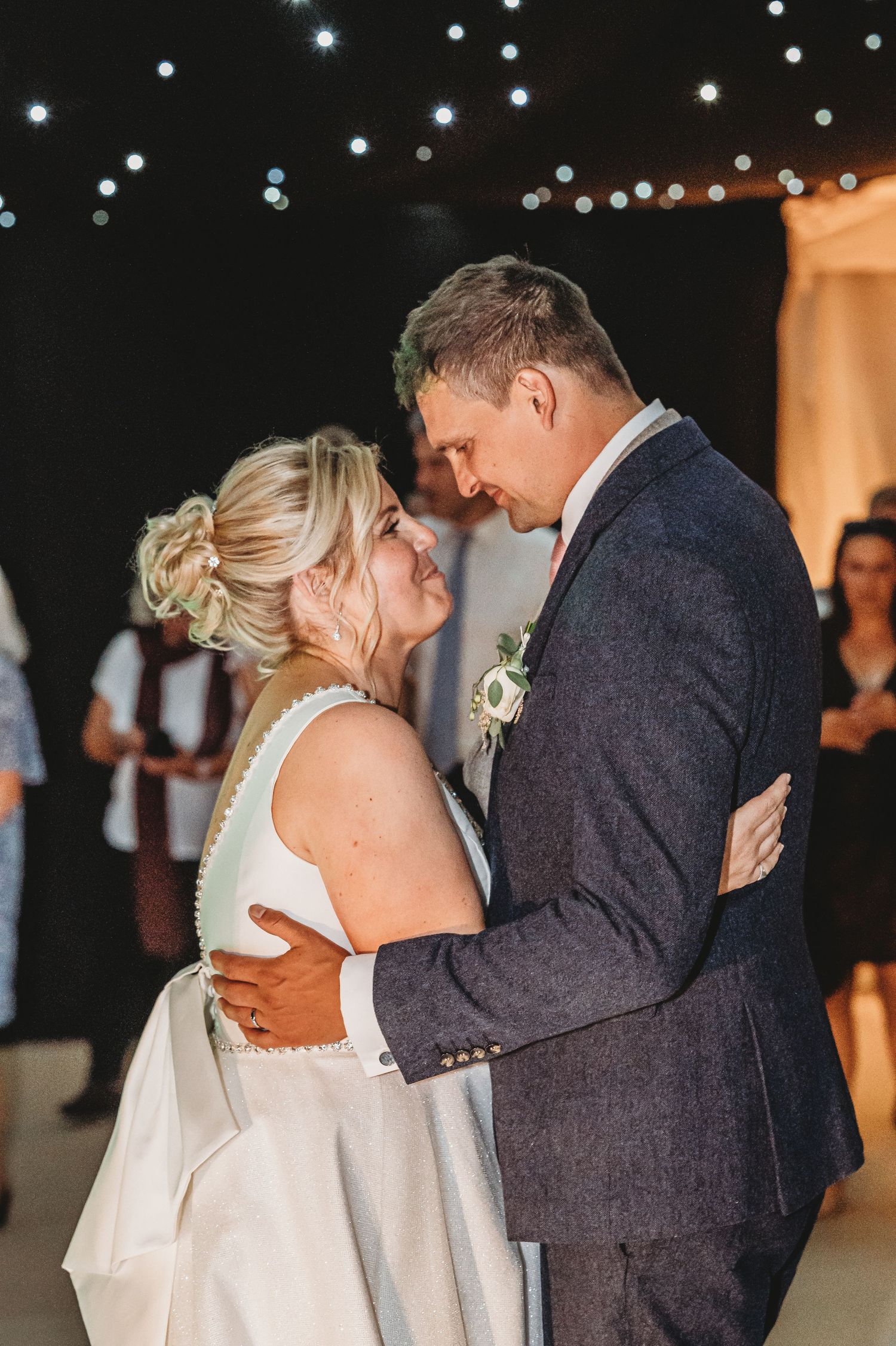 A romantic first dance moment at a wedding reception with twinkling lights overhead creating a magical atmosphere.