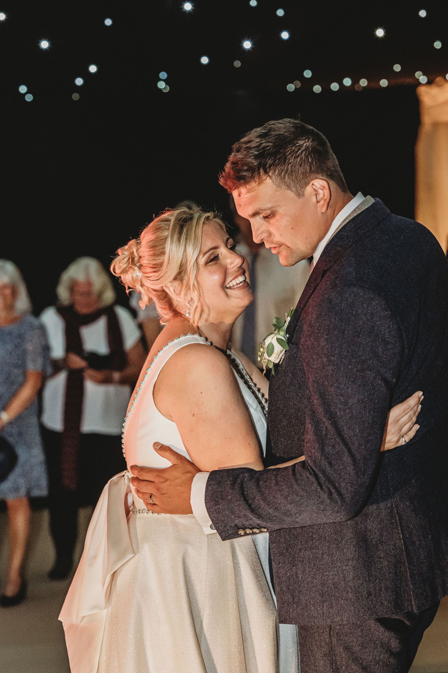 A couple shares a romantic dance moment under twinkling lights at their wedding reception.