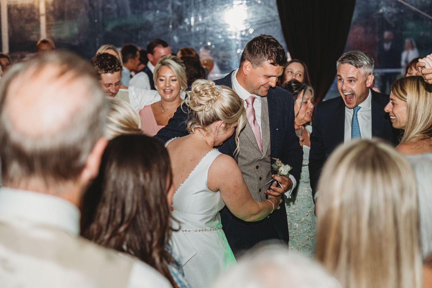Wedding guests dance together on a crowded dance floor during an evening reception celebration.