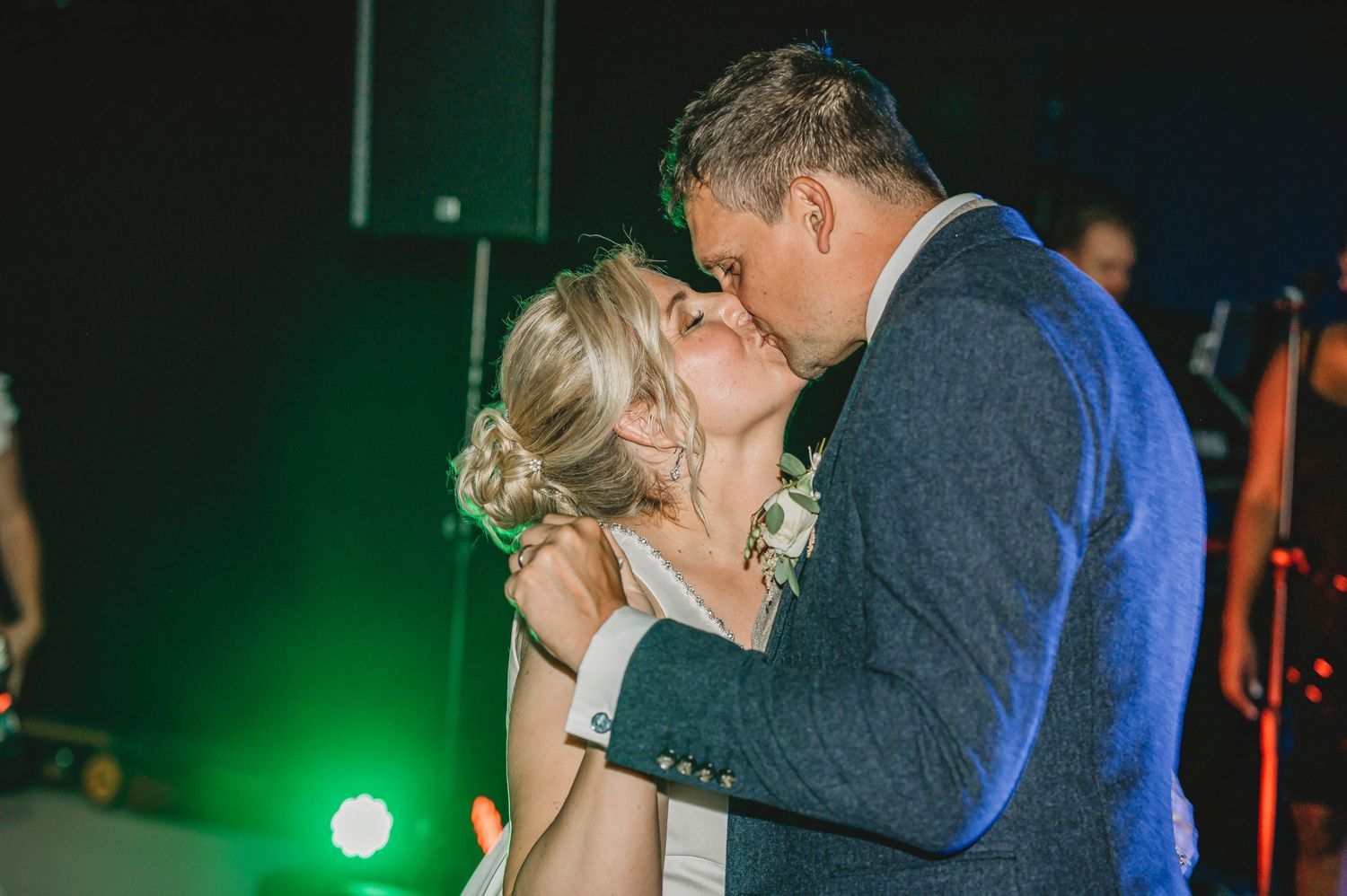 A couple shares a romantic kiss on a dance floor with green stage lighting in the background.