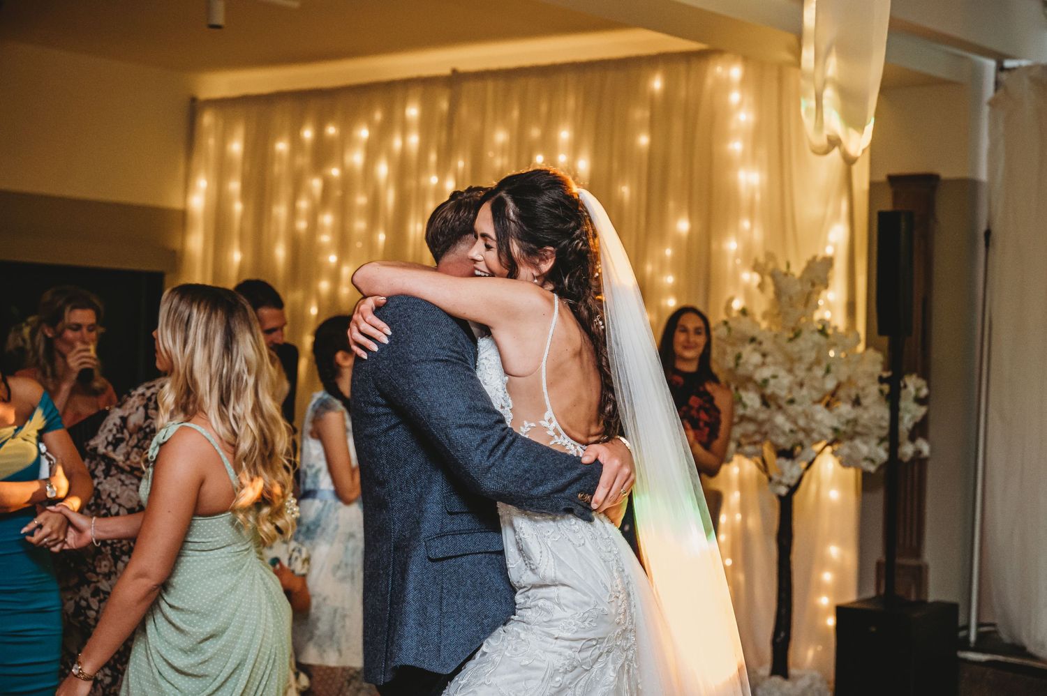 A couple shares their first dance at a wedding reception with string lights glowing in the background.
