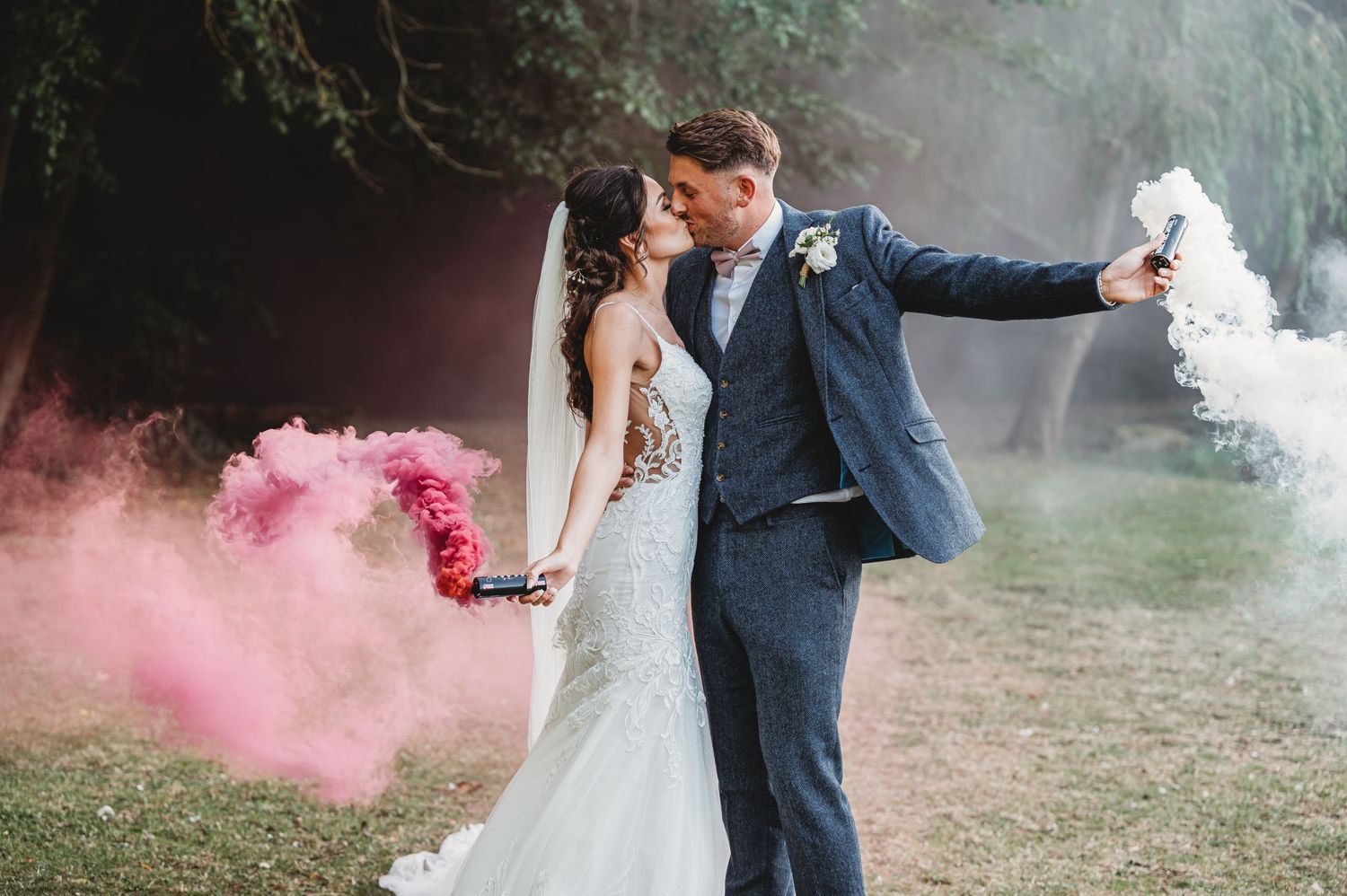 A couple releases colorful smoke bombs during their outdoor wedding photoshoot in a misty forest setting.