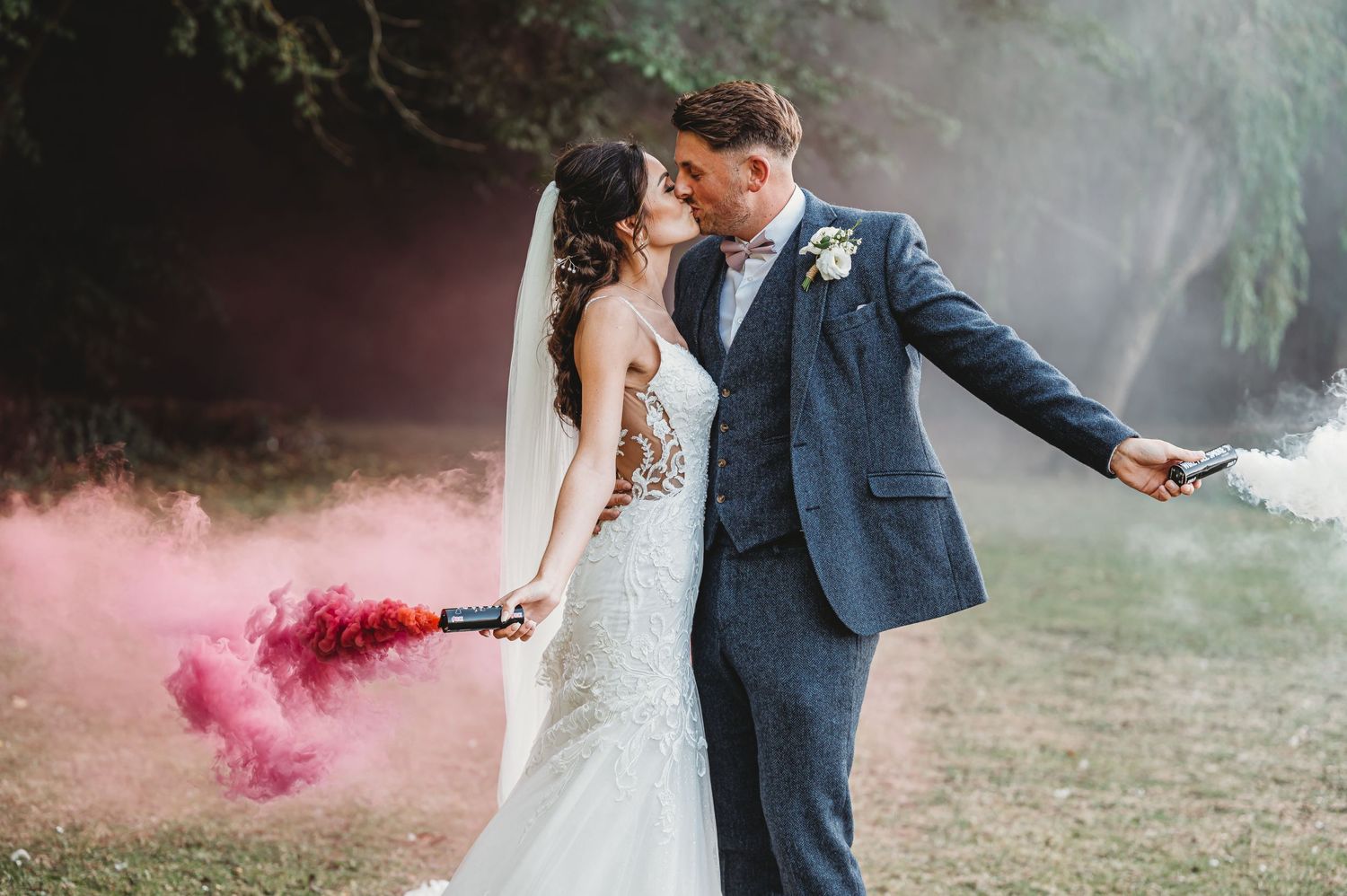A bride and groom pose outdoors with pink smoke bombs creating a romantic and ethereal atmosphere.