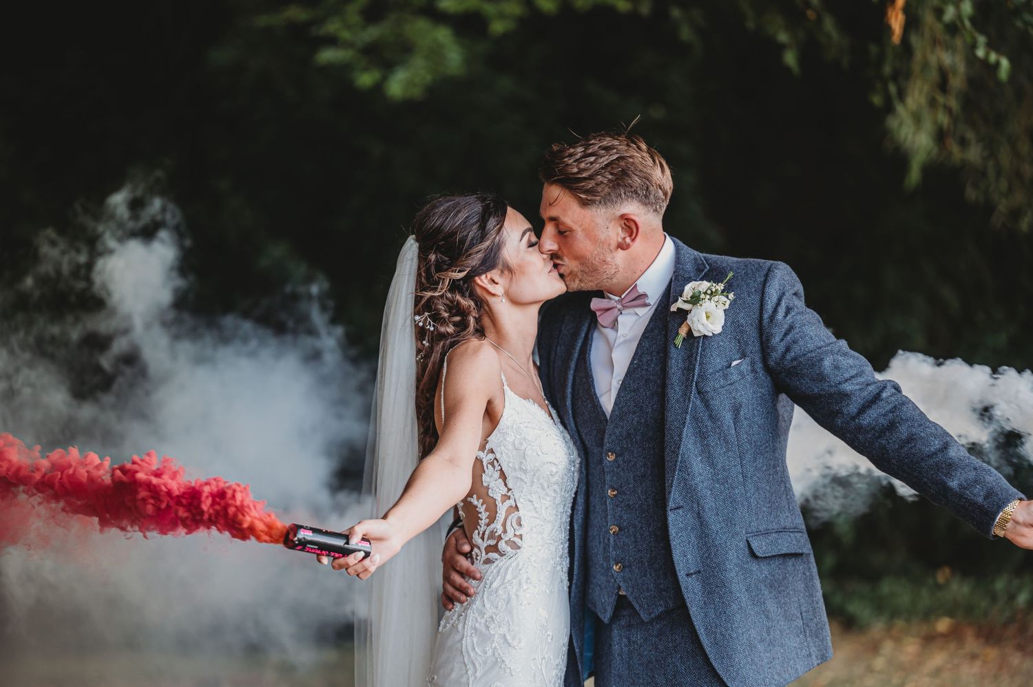 A couple shares a romantic moment with red smoke bombs at their outdoor wedding celebration.