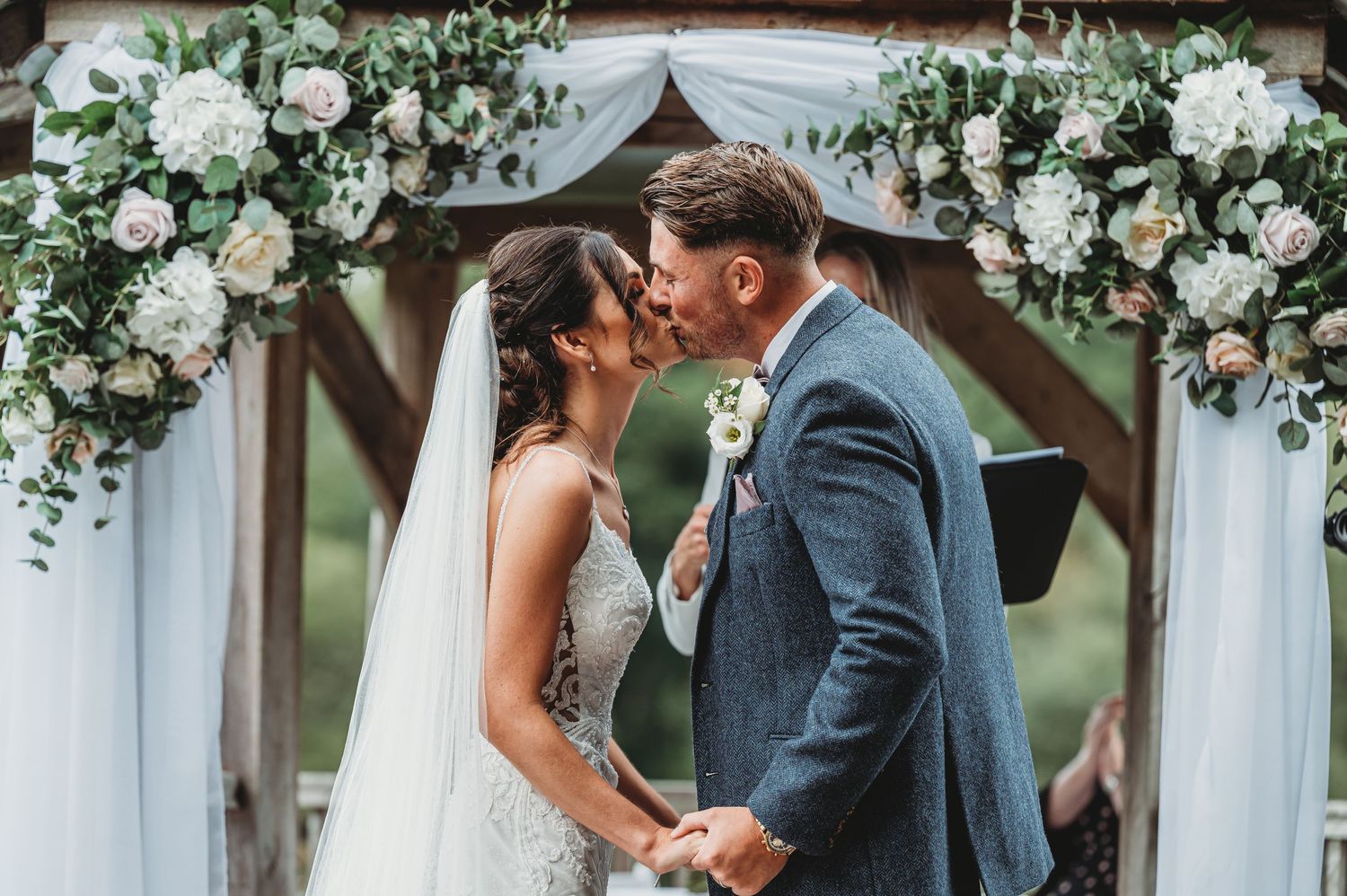 A romantic wedding ceremony moment under a floral arch decorated with white roses and cascading greenery.