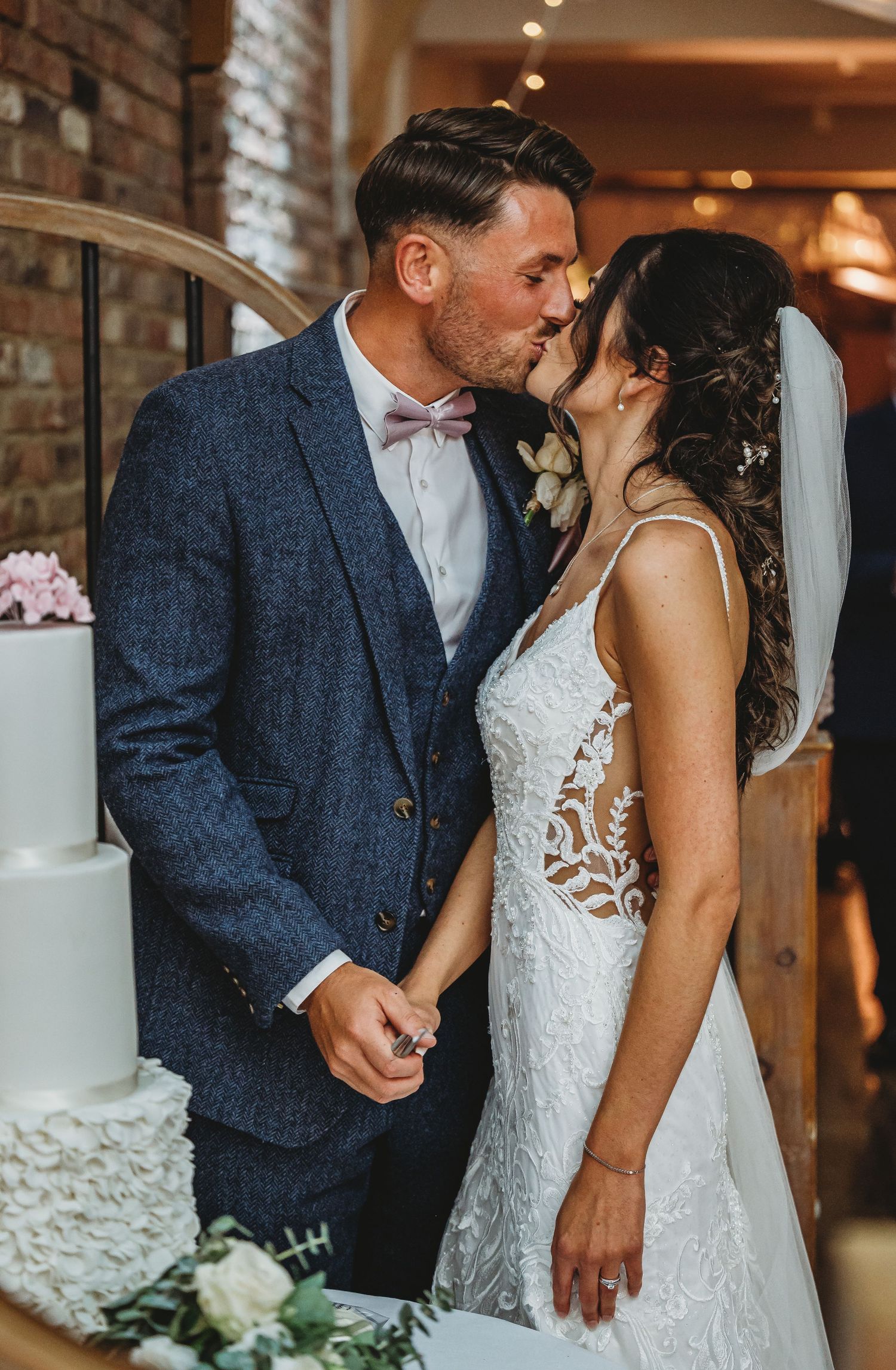 Newlyweds share an intimate moment beside their elegant white wedding cake decorated with roses.