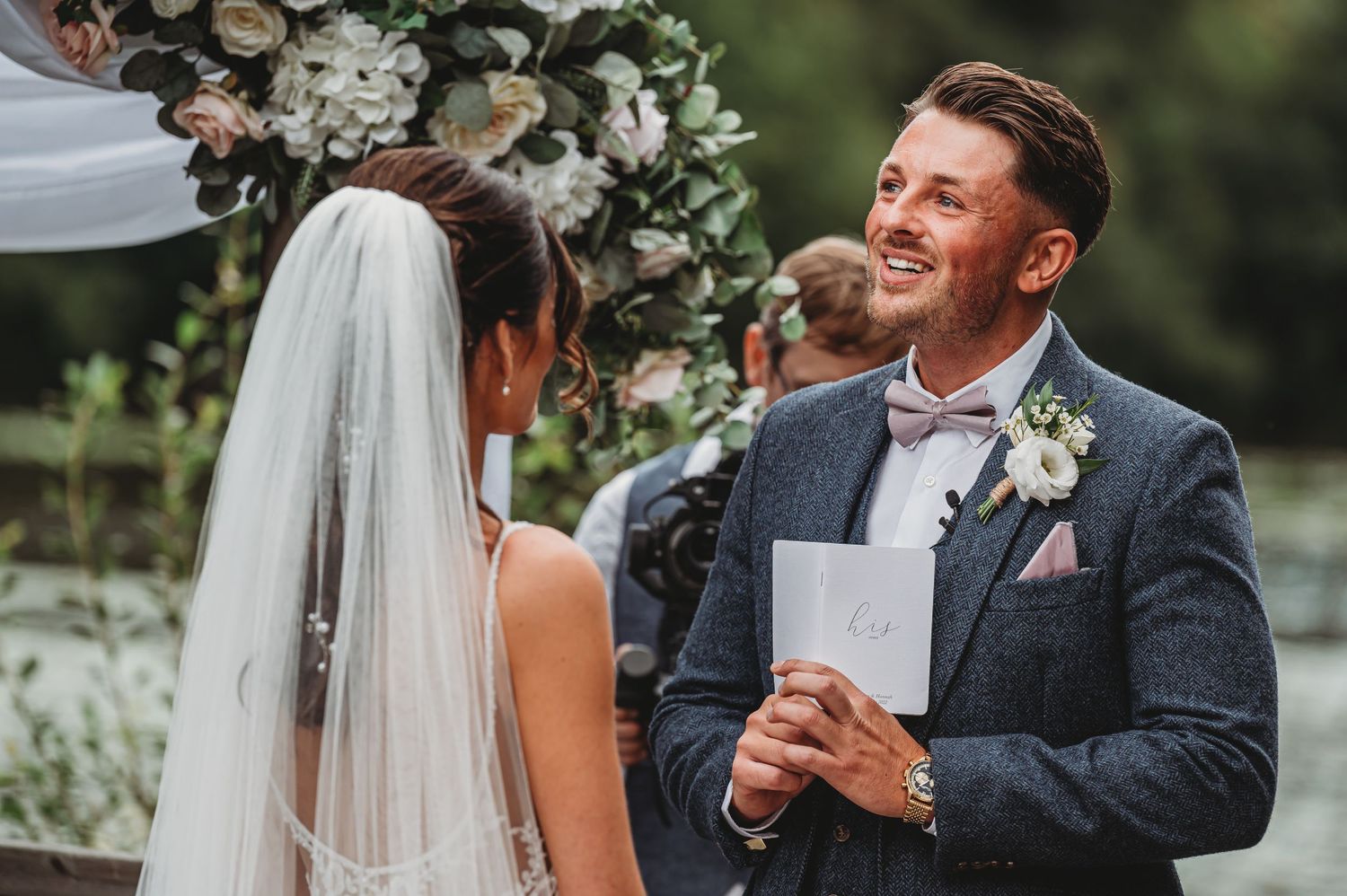 A couple exchanges vows under a floral arch during an outdoor wedding ceremony.